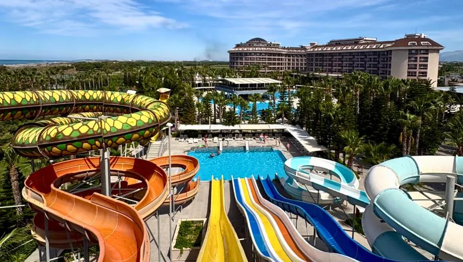 Waterpark van Sunmelia Beach Resort met kleurrijke glijbanen, zwembaden en tropische palmbomen. Vanuit dit overzicht is goed te zien dat het resort uitgebreide faciliteiten biedt voor gezinnen en liefhebbers van waterpret tijdens een all inclusive vakantie aan de Turkse Rivièra.
