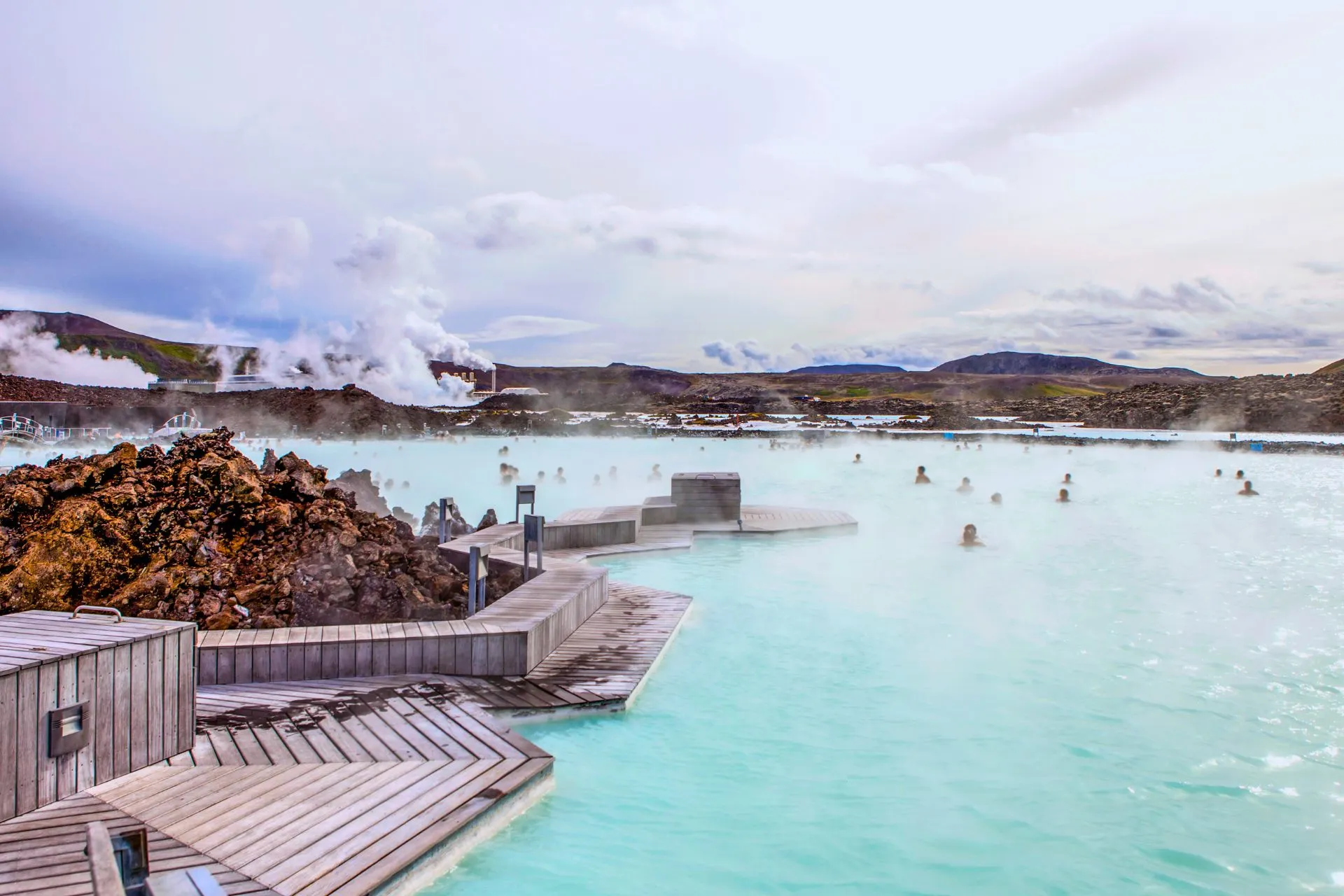 Overzicht van de Blue Lagoon in IJsland, met helderblauw geothermisch water, houten platforms en stoom die opstijgt uit de omringende lavavelden.