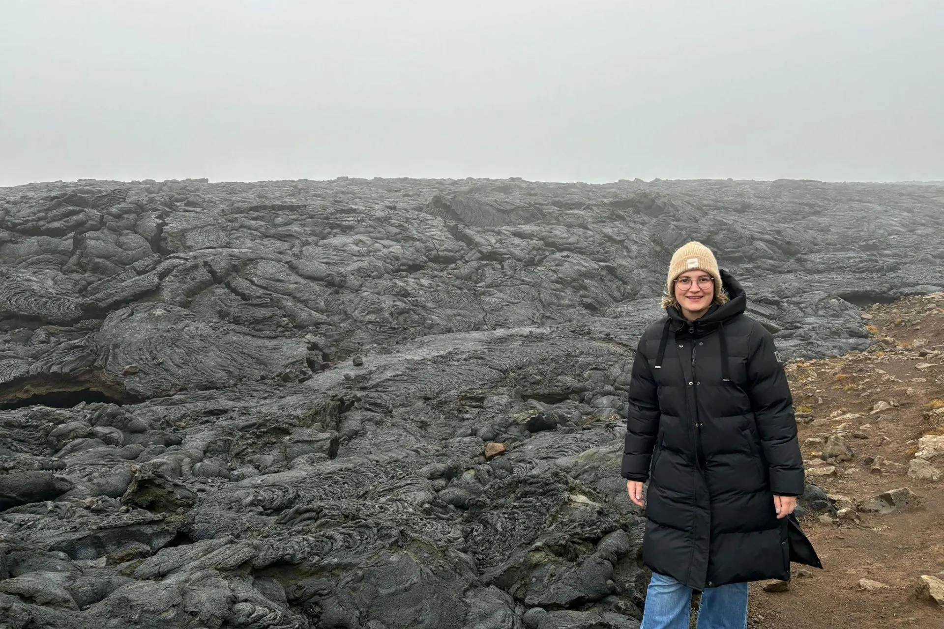 Reisadviseur Vera poseert bij een veld van gestolde zwarte lava in een mistig landschap in Reykjanes, IJsland.