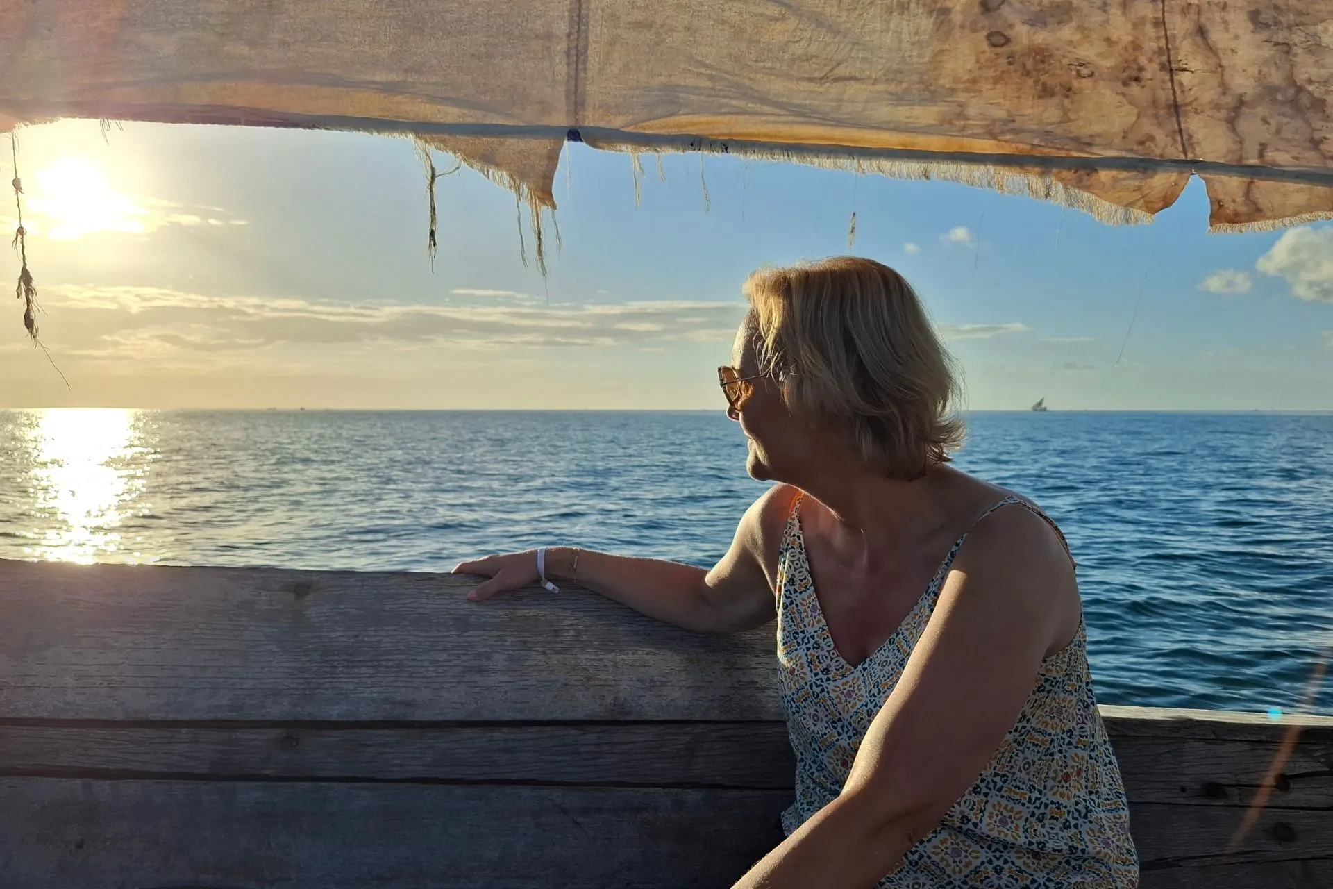 Reiziger geniet van een traditionele dhowcruise voor de kust van Zanzibar terwijl de zon langzaam ondergaat boven de Indische Oceaan. Vanaf het houten zeilschip biedt het uitzicht op het kalme, azuurblauwe water een onvergetelijke ervaring. Een dhowcruise is een van de populairste excursies tijdens een vakantie op Zanzibar.