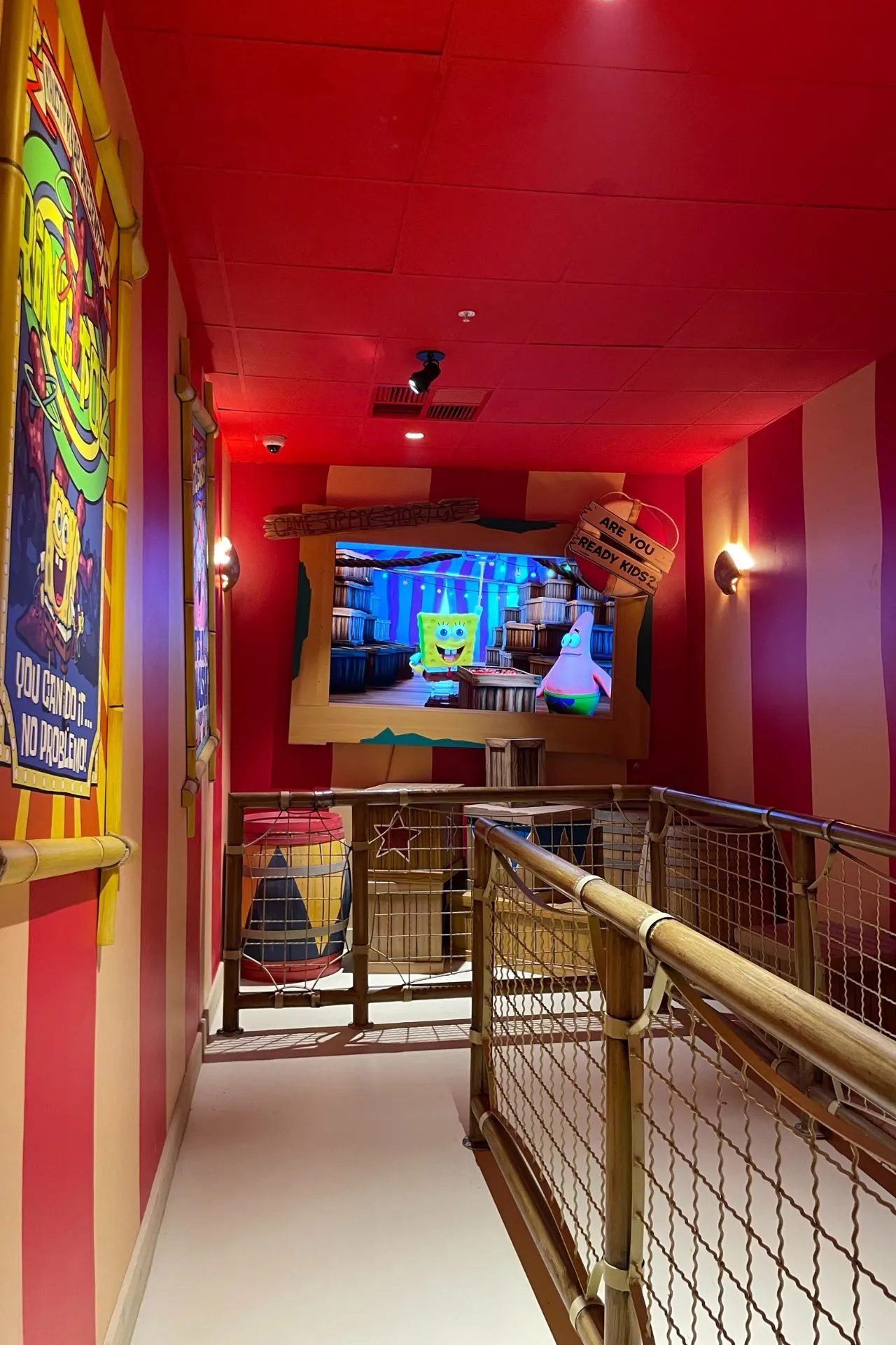  Gang met rode muren en een speelstructuur van touwen, inclusief SpongeBob-decor en een scherm met animaties.