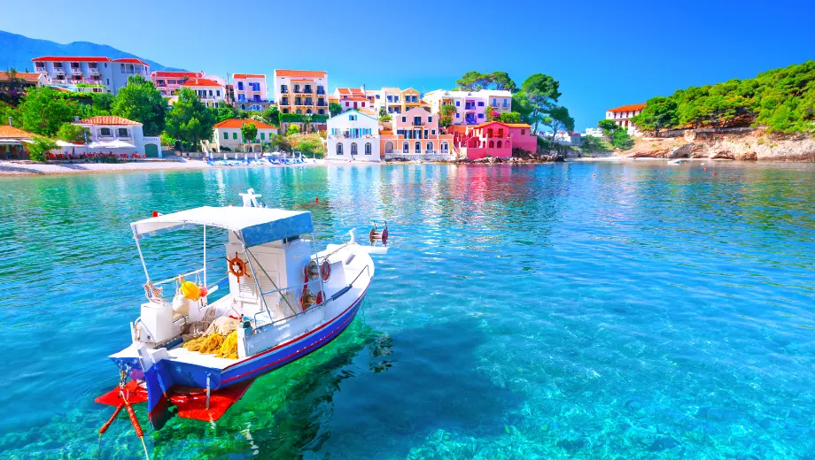 Deze afbeelding toont een idyllisch kustdorp met kleurrijke huizen aan het water, perfect voor een zonvakantie Verasole. Op de voorgrond dobbert een kleine witte boot op het heldere, turquoise water, wat direct het ultieme vakantiegevoel oproept. De zon schijnt fel en de lucht is strakblauw, ideaal voor een ontspannen Verasole vakantie. De pittoreske omgeving en het rustige water maken deze locatie zeer geschikt voor een pakketreis Verasole naar de Middellandse Zee. Of je nu kiest voor een romantische vakantie, een gezinsuitje of een avontuurlijke reis, bij Verasole vind je altijd de perfecte zonbestemming. Deze afbeelding benadrukt het gemak en de sfeer van Verasole vakanties: alles is tot in de puntjes geregeld, van vlucht tot accommodatie. Boek jouw Verasole vakantie en geniet van een zorgeloze zonvakantie in een sfeervol dorp aan het water, waar ontspanning en plezier centraal staan.