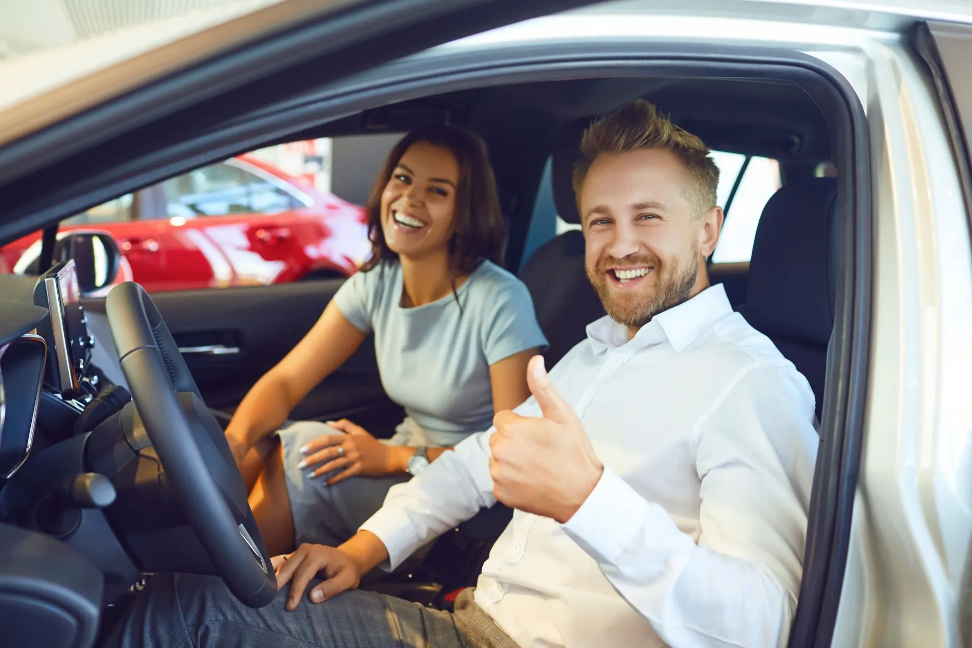 Man en vrouw zitten in hun huurauto, de man steekt zijn duim op van tevredenheid met hun autoverhuur.