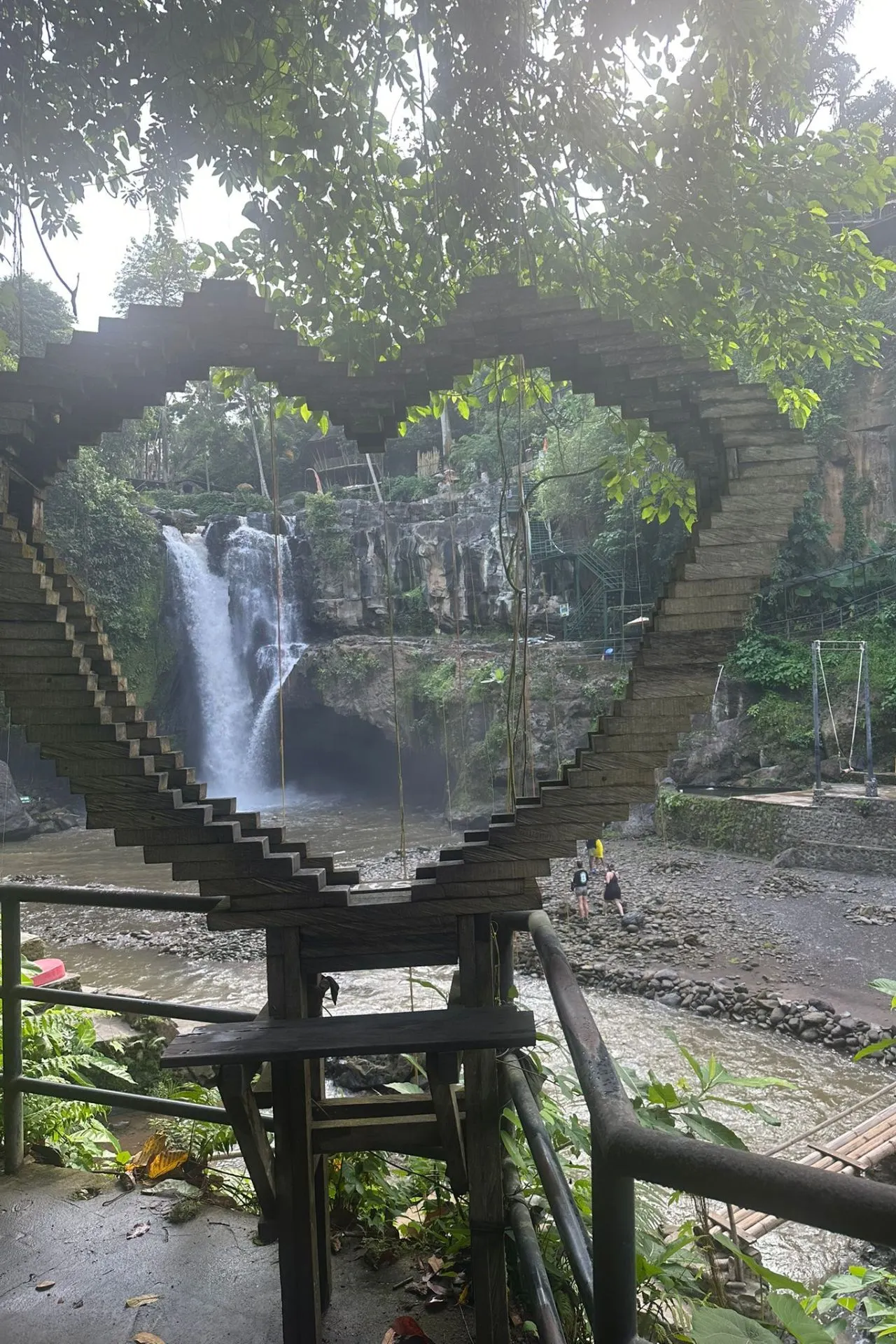 Prachtige waterval omlijst door een houten hartvormige structuur, omringd door weelderig groen.