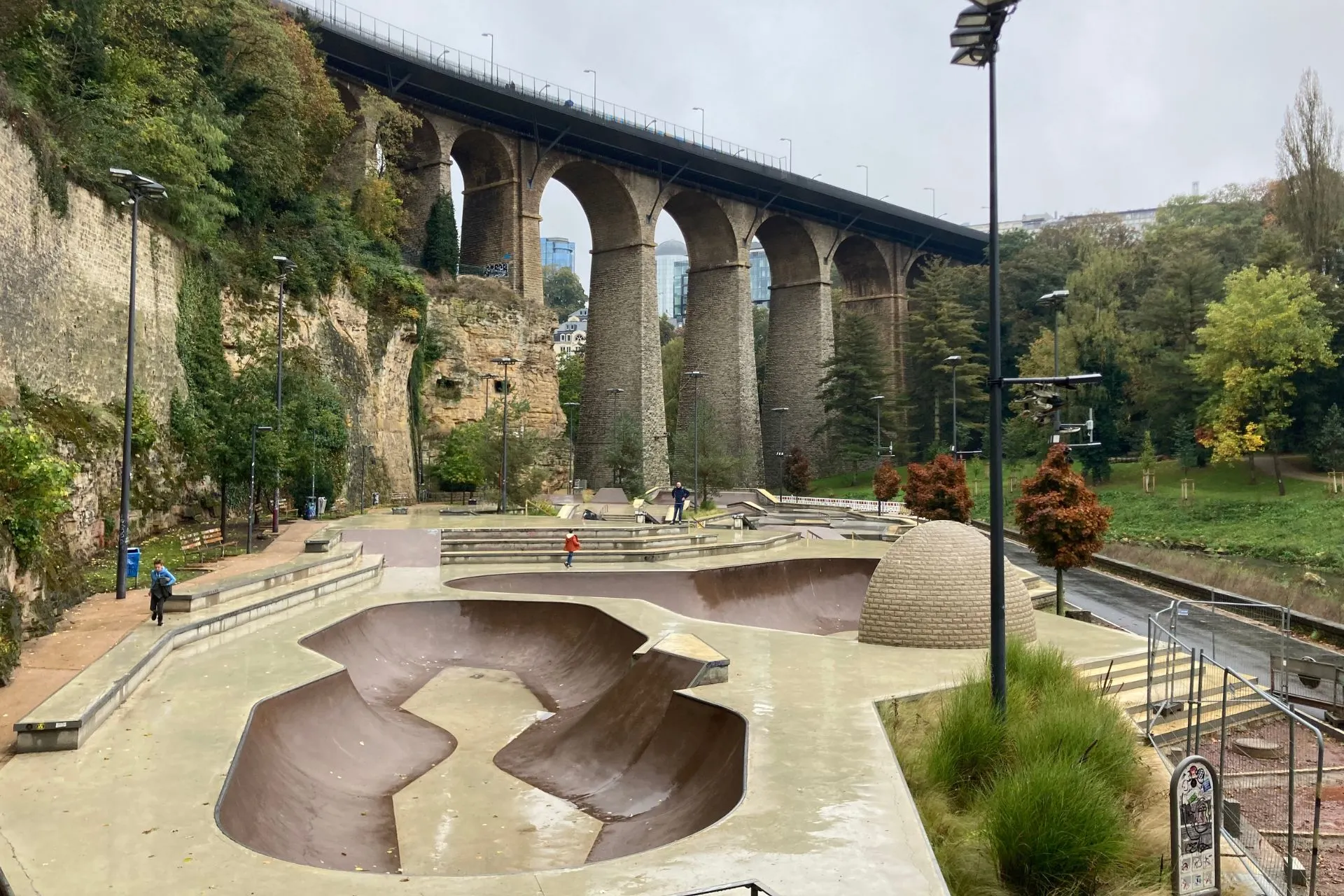 Een skatepark met betonnen ramps en een historische stenen brug op de achtergrond in Luxemburg Stad.