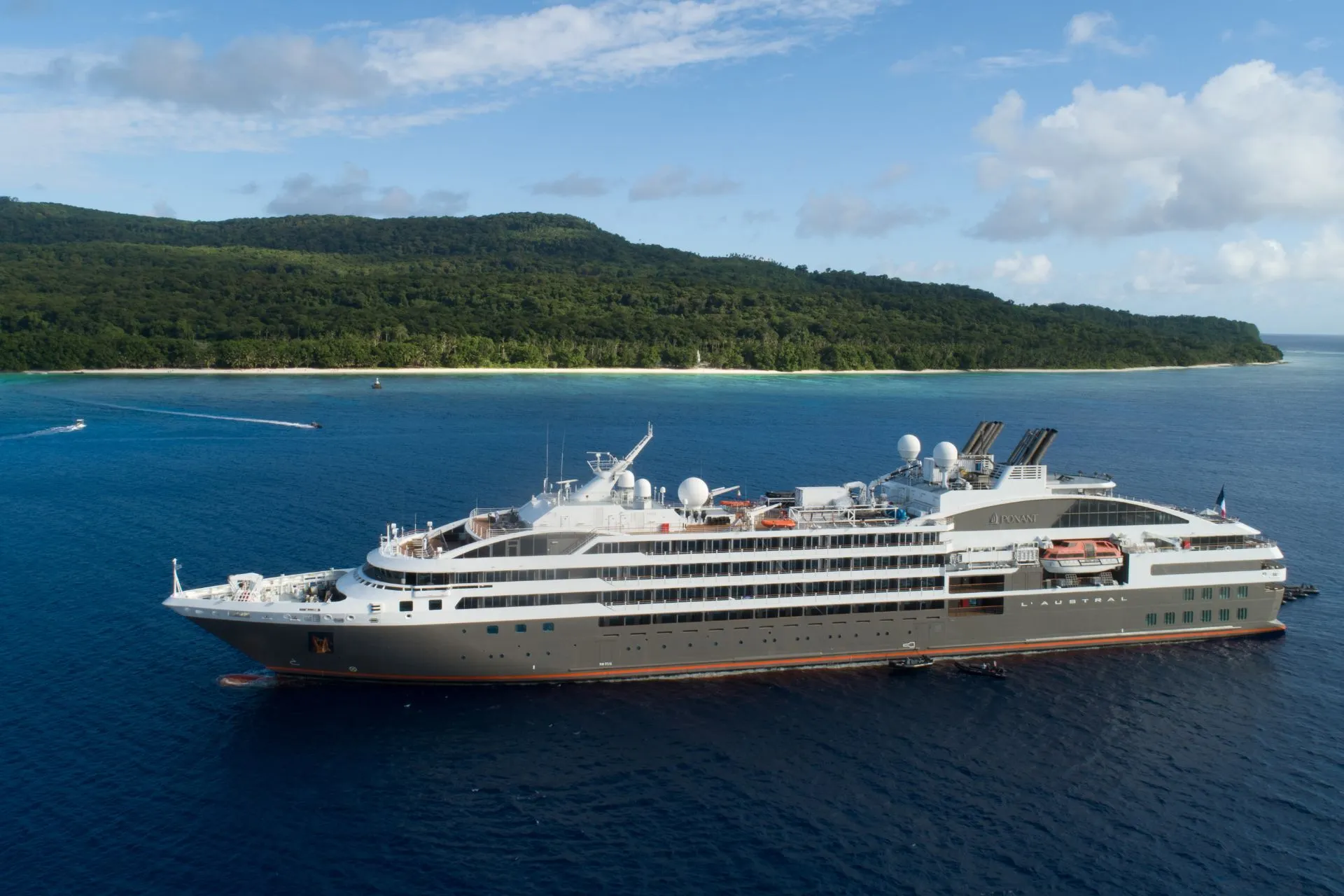 Een modern Ponant expeditieschip vaart langs een groene kustlijn. Deze luxe cruises combineren comfort, innovatieve schepen en bijzondere bestemmingen, ver weg van de massa.
