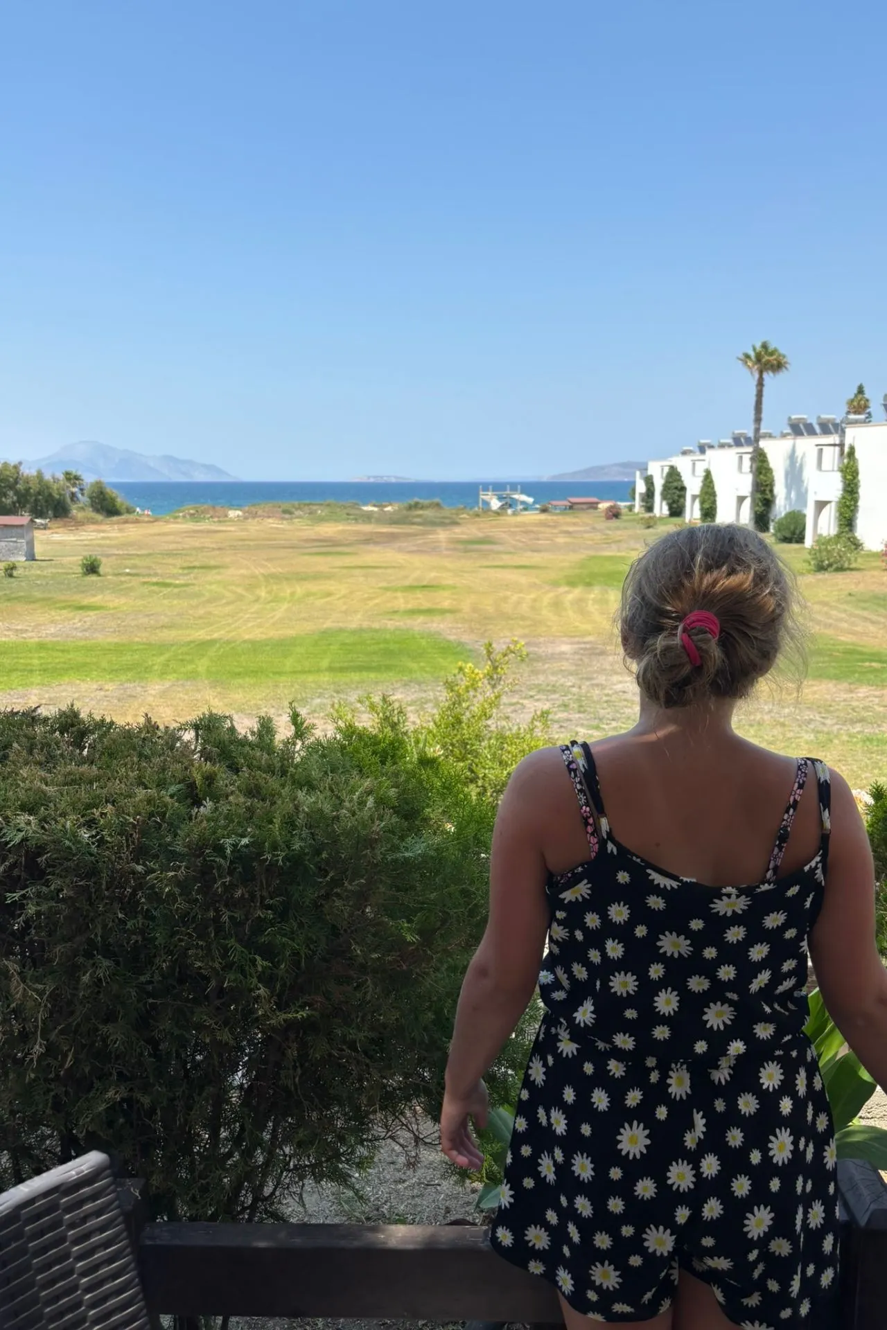 Meisje kijkt vanaf het Gaia Royal resort uit over een open grasveld richting de helderblauwe zee en bergachtige eilanden in de verte

