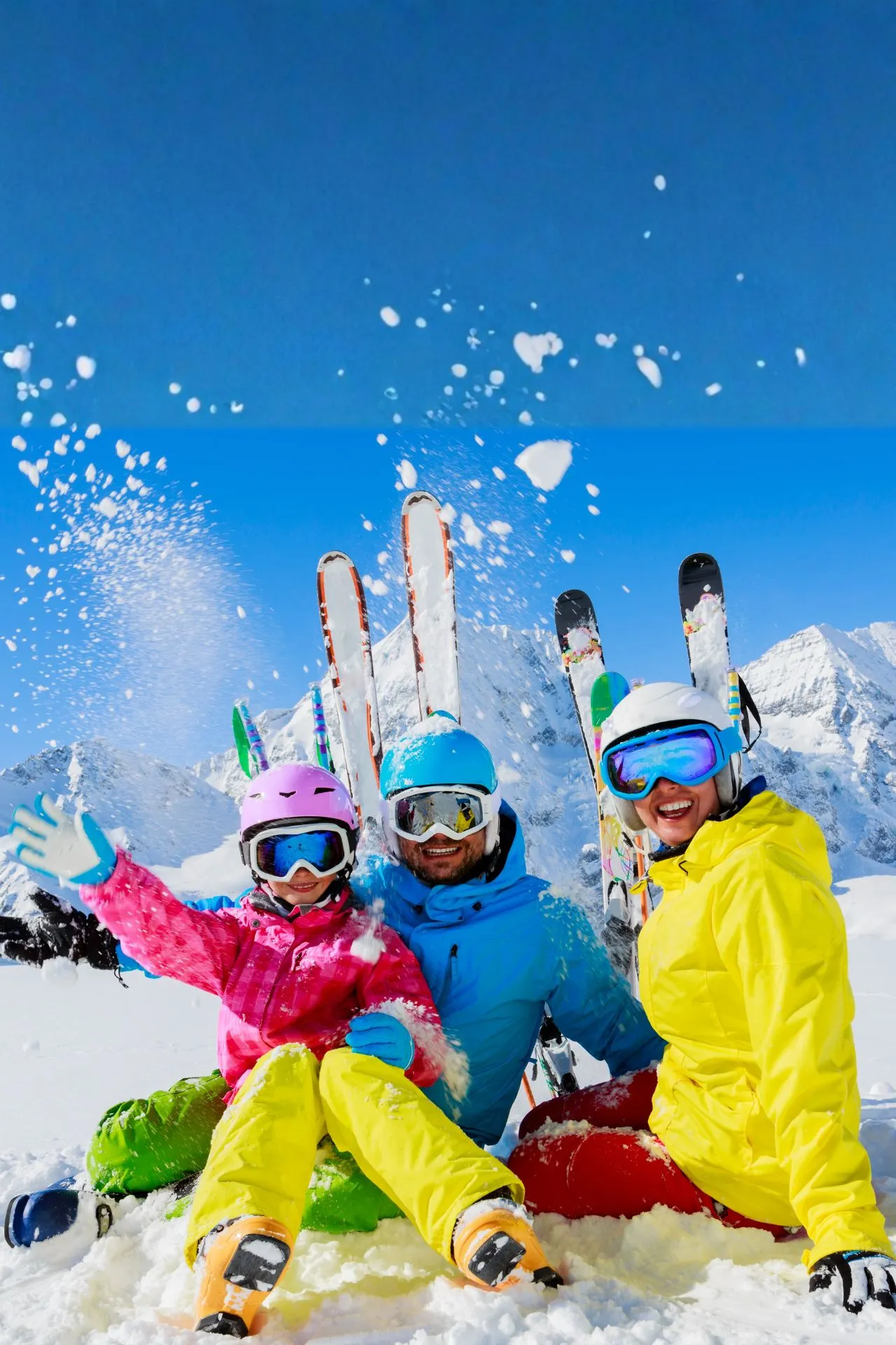 Drie personen in kleurrijke skikleding liggen speels in de sneeuw op een zonnige dag in de bergen, omringd door indrukwekkende besneeuwde bergtoppen en een helderblauwe lucht. Ski’s staan rechtop in de sneeuw op de achtergrond, wat een actieve wintersportvakantie benadrukt. Perfecte bestemming voor skiën, snowboarden en winterplezier in een adembenemend berglandschap, ideaal voor een actieve kerstvakantie of winteruitje in de Alpen.