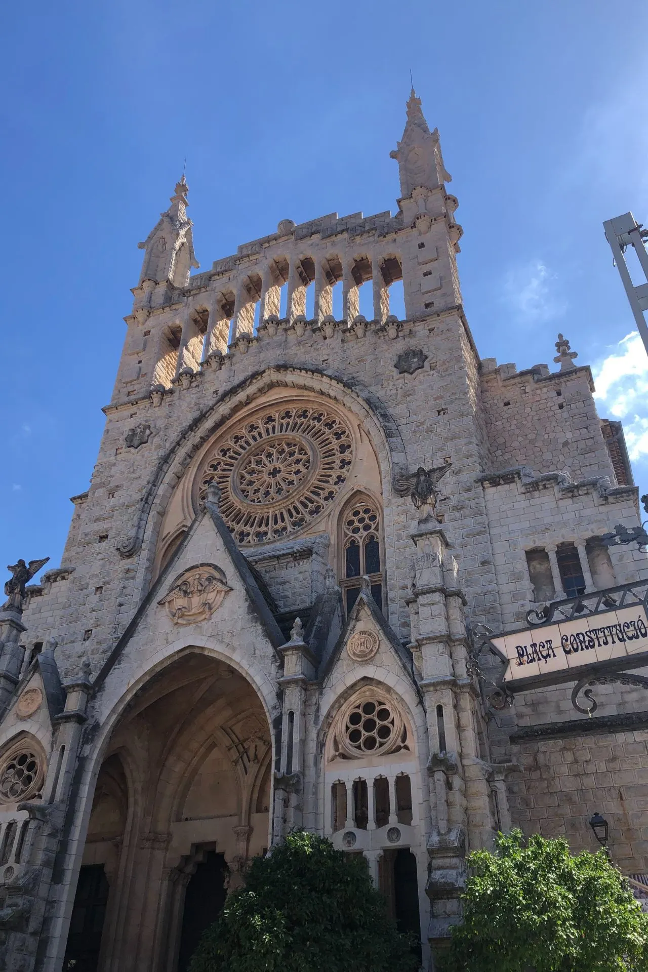 Indrukwekkende gevel van de kerk Sant Bartomeu op het stadsplein van Sóller, Mallorca, met gedetailleerde architectuur en een prachtig roosvenster onder een heldere blauwe lucht. Sóller is een historisch dorp in de Serra de Tramuntana, bekend om zijn charmante straatjes, gezellige pleinen en authentieke Spaanse sfeer. Populaire bestemming voor een dagtrip tijdens een vakantie op Mallorca.
