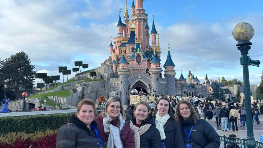 Een groep vriendinnen poseert lachend voor het iconische Kasteel van Doornroosje in Disneyland Parijs. Ze staan op het kleurrijke plein van Disneyland Park, omringd door bloemen en bezoekers. De blauwe lucht en het sprookjesachtige kasteel creëren echte Disney-magie. De foto straalt plezier, vakantiegevoel en een dag vol attracties, parades en avontuur in het populaire pretpark Disneyland Parijs uit.