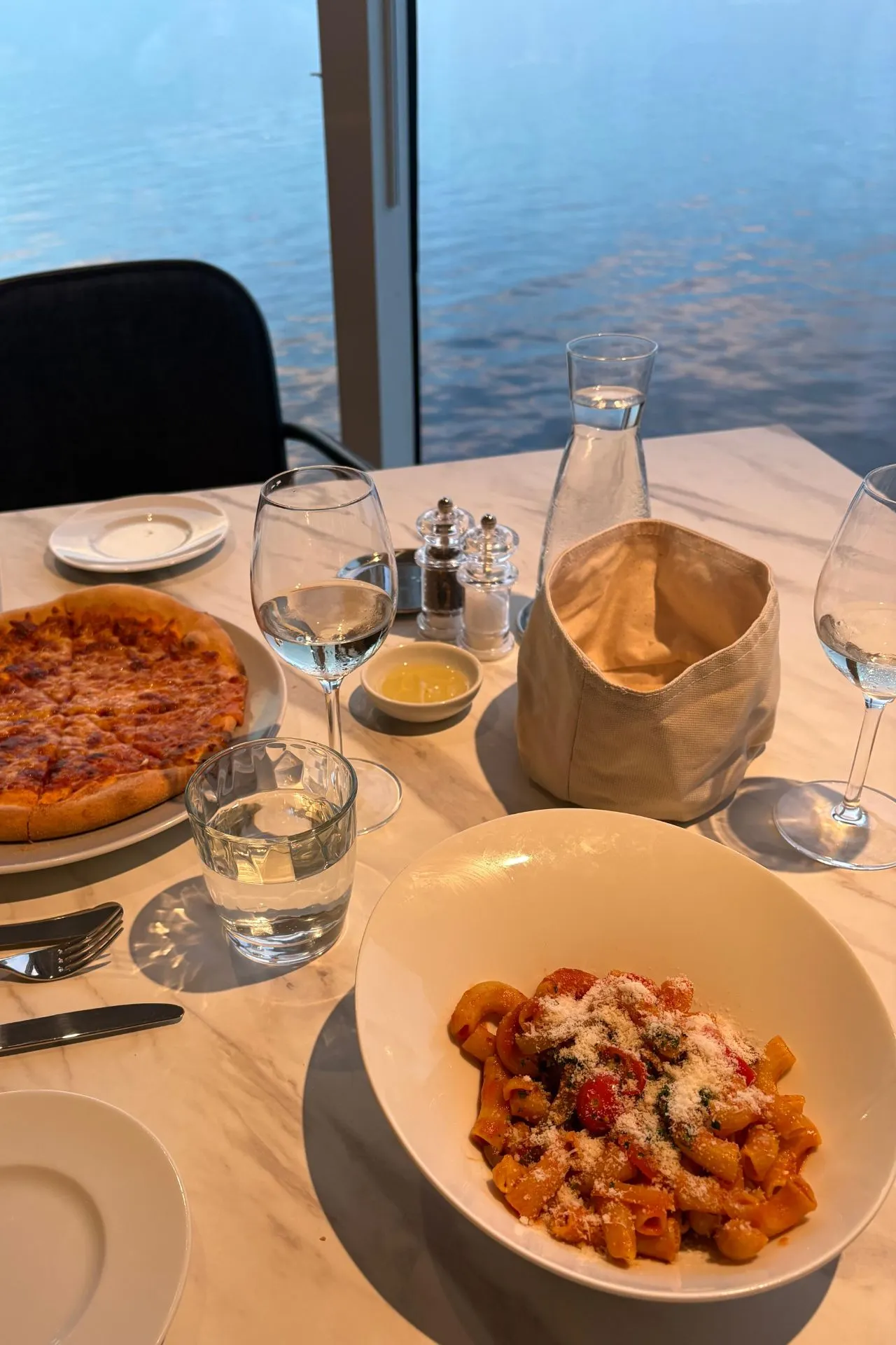 Maaltijd in een restaurant aan boord van de Mein Schiff Flow met pasta, pizza en uitzicht over zee. Op het cruiseschip zijn diverse inbegrepen restaurants aanwezig waar gasten kunnen genieten van internationale gerechten. Dankzij de grote ramen combineer je tijdens het diner culinaire verwennerij met een prachtig uitzicht over het water.