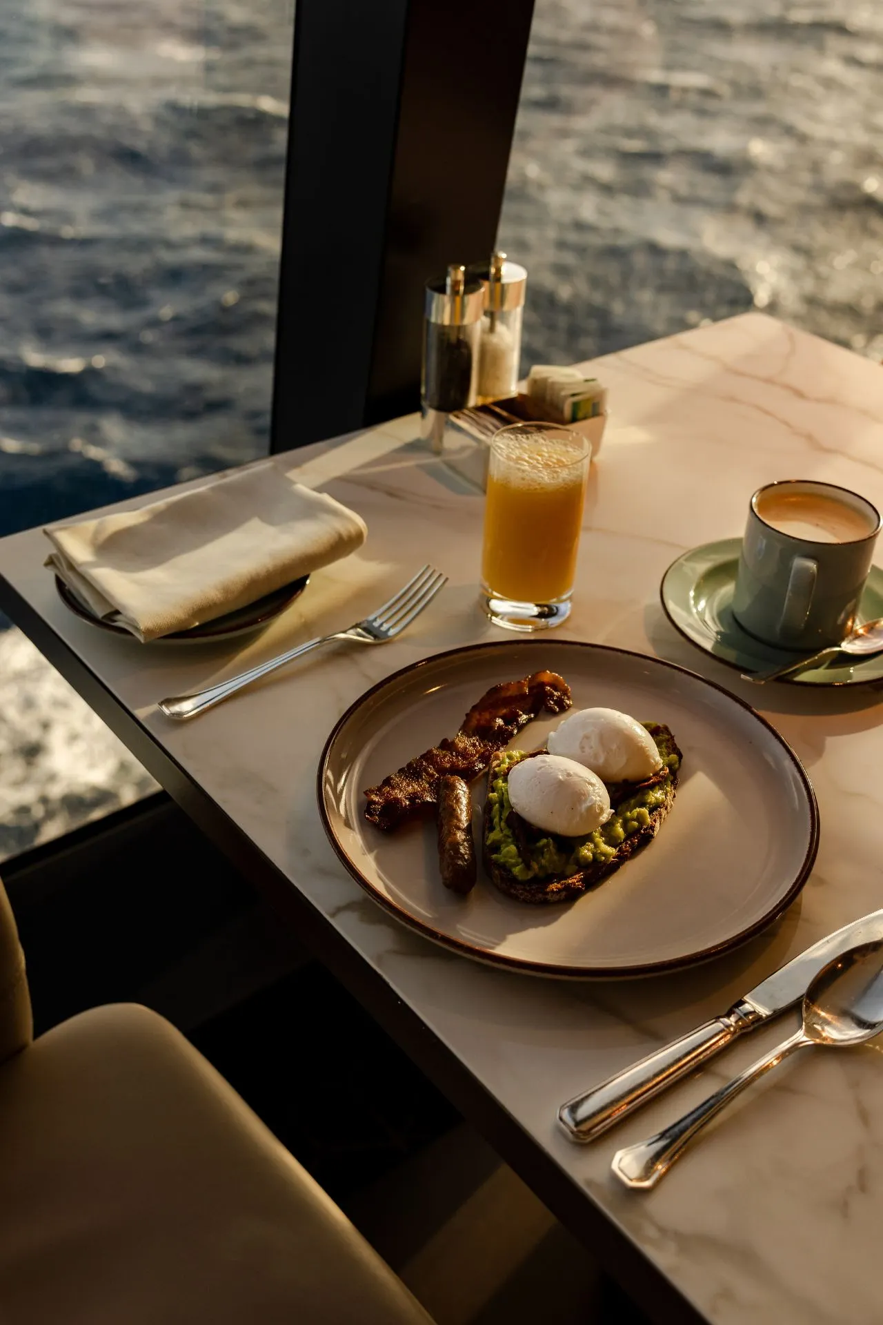 Ontbijt aan boord van een Explora Cruise schip, stijlvol gepresenteerd op een marmeren tafel met uitzicht op de oceaan. Het gerecht bevat gepocheerde eieren, toast en gegrilde groenten, vergezeld van een glas vers sinaasappelsap en een kop koffie. Deze foto benadrukt de verfijnde culinaire ervaring en premium service die Explora Journeys biedt tijdens een luxe cruisevakantie. Ideaal voor reizigers die gastronomie, comfort en exclusiviteit op zee waarderen.
