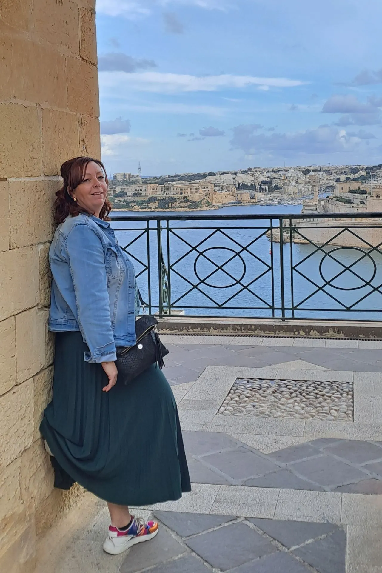 Reisadviseur Joyce, leunend tegen een muur met uitzicht op het water in Valetta.
