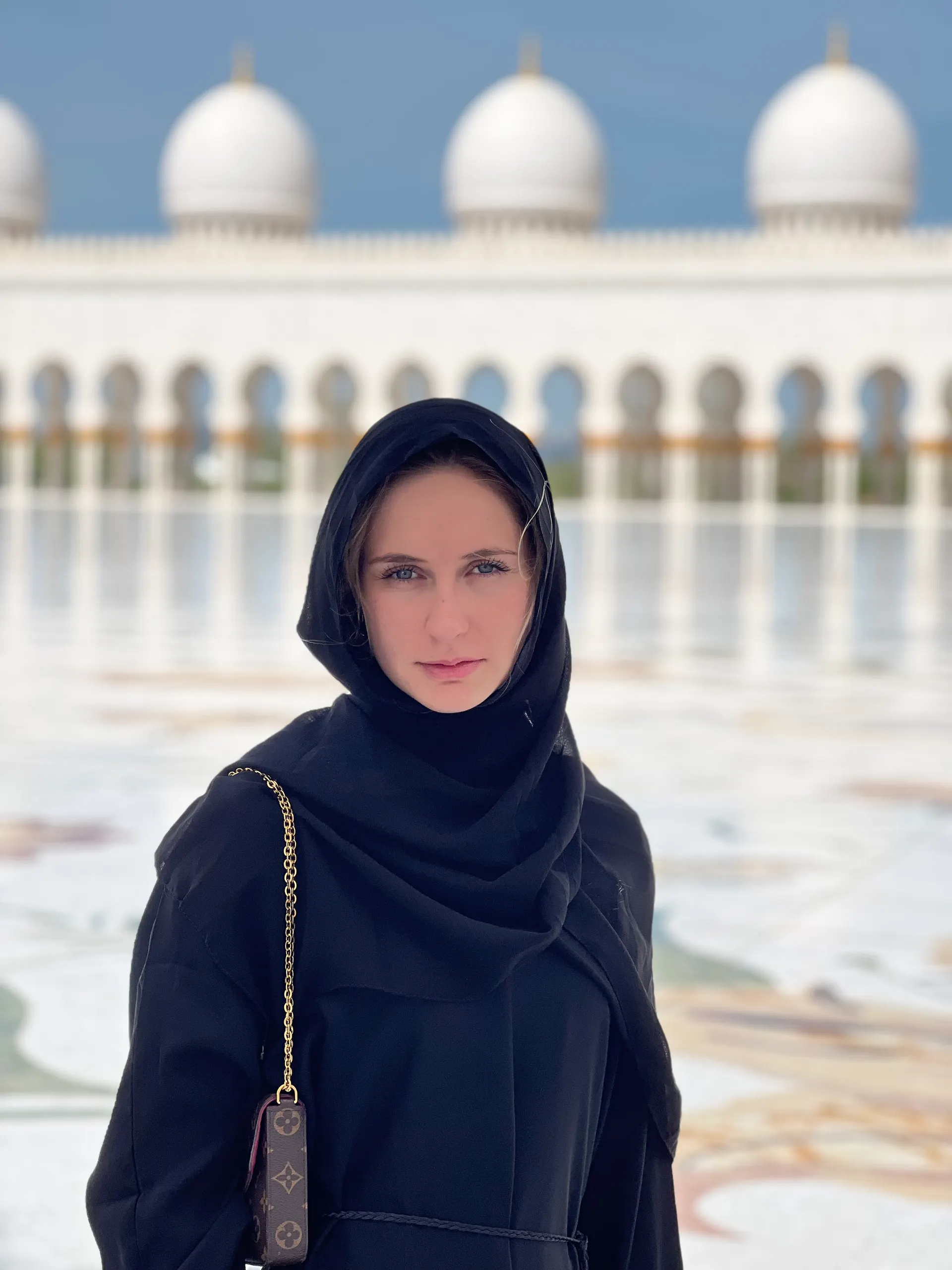 Emmie is in Dubai, gekleed in zwart, met de beroemde moskee op de achtergrond, omringd door de rust en schoonheid van de omgeving.