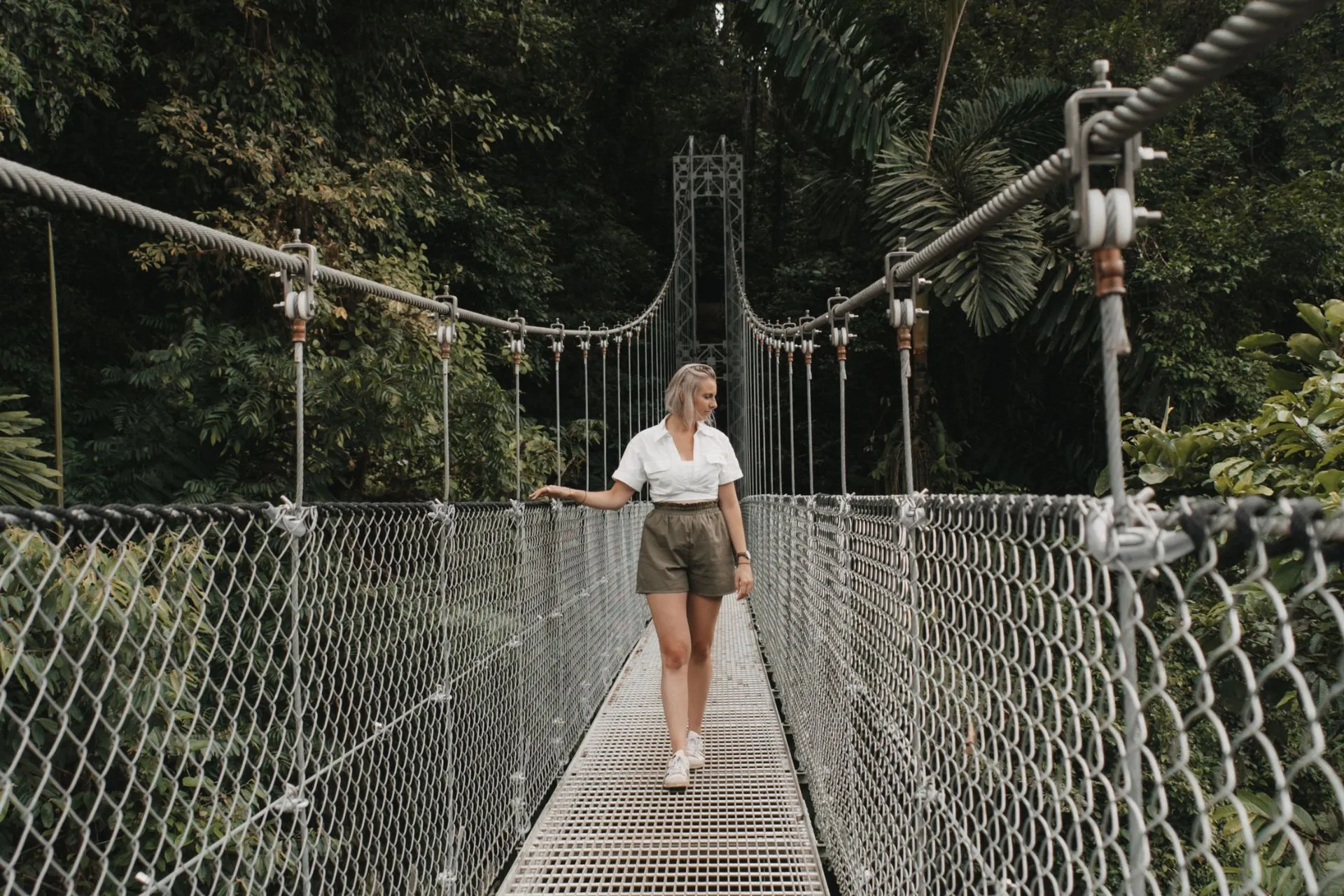 Een vrouw loopt ontspannen over een hangbrug midden in de groene jungle van Costa Rica, omringd door dichte vegetatie.