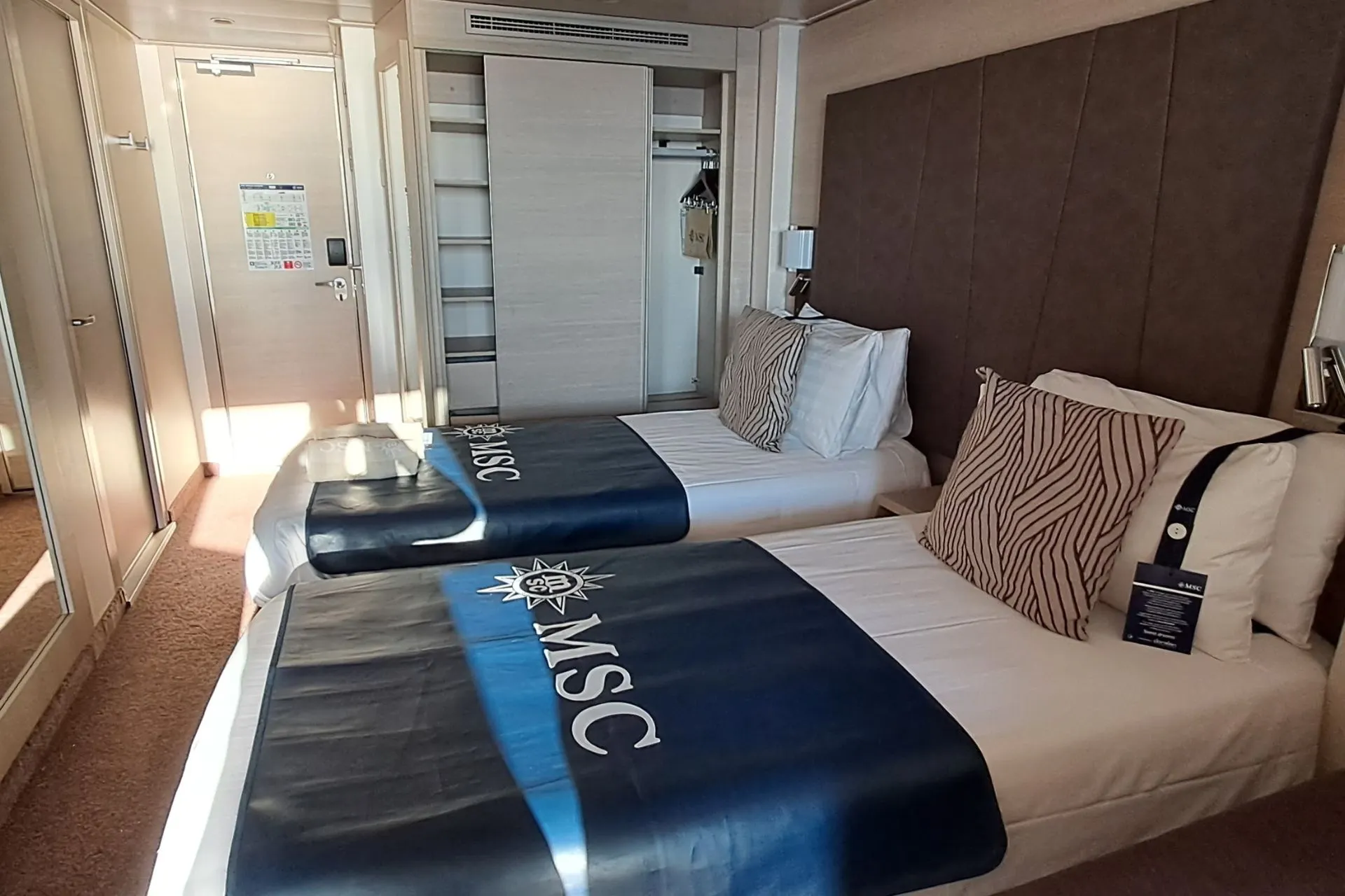 Interieur van een MSC Cruises hut met twee aparte bedden, voorzien van MSC-bedspreads, een spiegelkast en moderne inrichting.