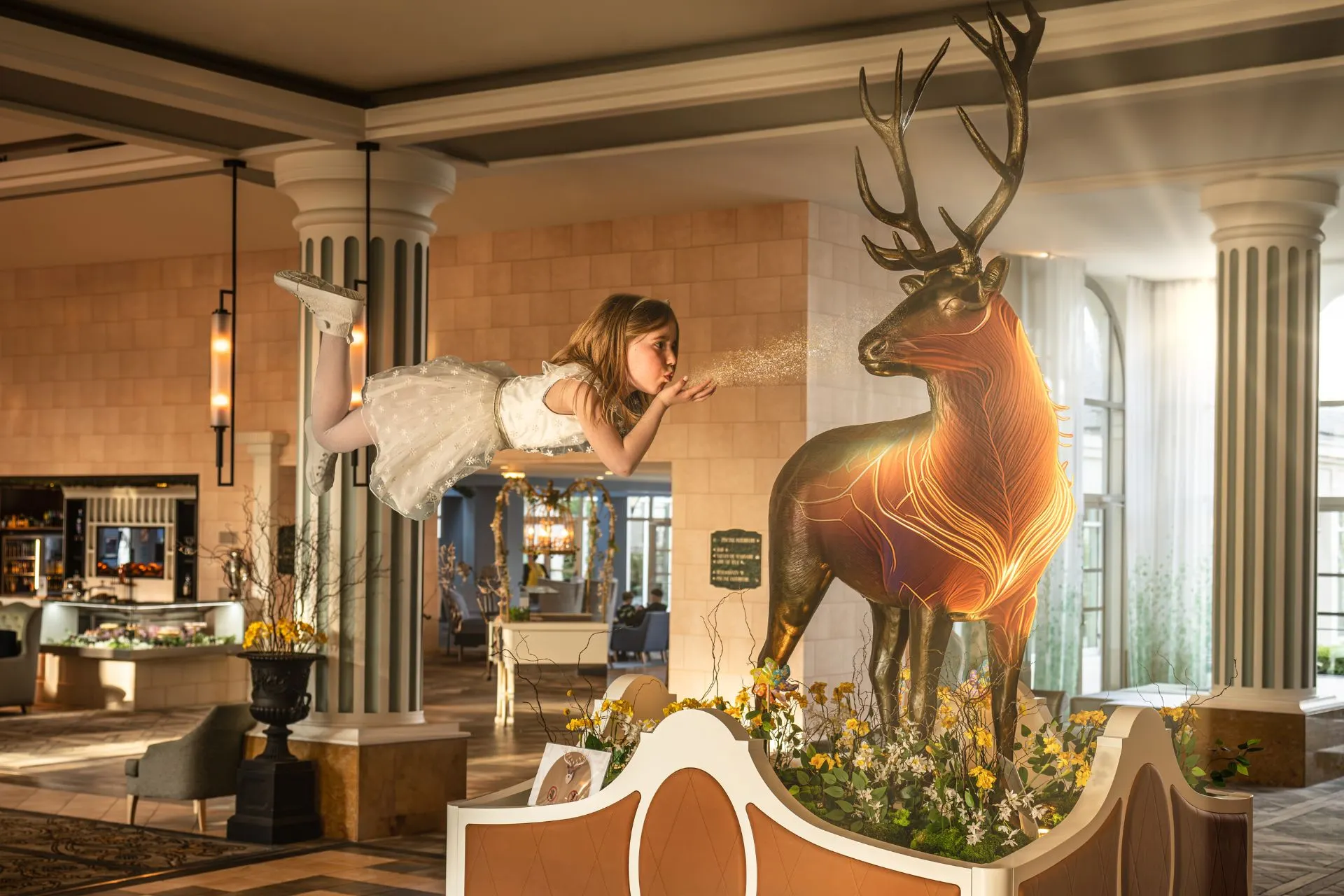 Magische decoratie in de lobby van het Dream Castle Hotel nabij Disneyland Parijs, met een groot bronzen hert versierd met lichtlijnen en een zwevende figuur in sprookjesstijl.