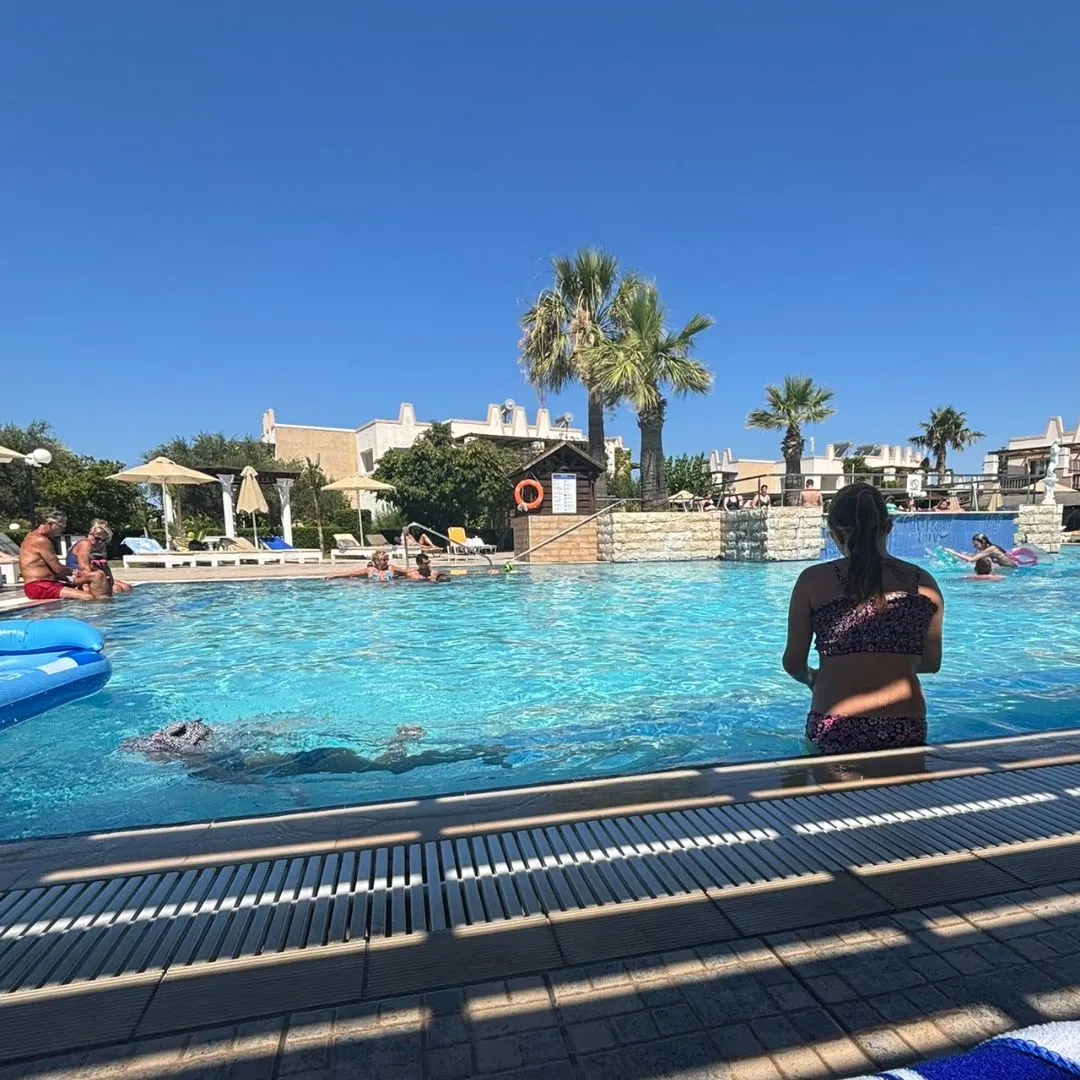 Kinderen en volwassenen genieten van een zonnige dag bij het zwembad van Gaia Royal Hotel op Kos, omringd door palmbomen en witte gebouwen