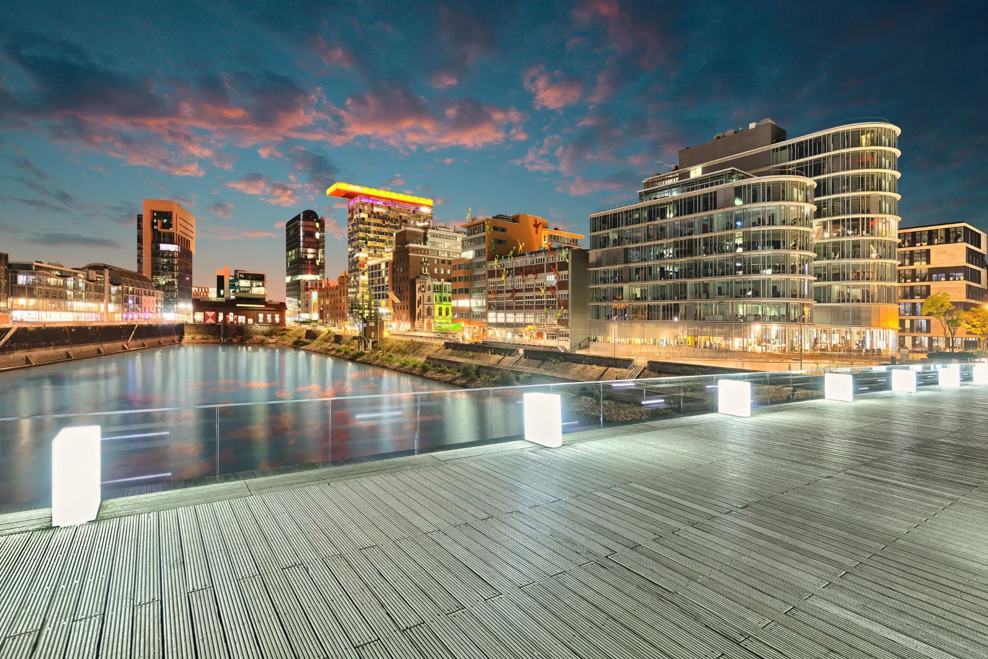 Skyline van Medienhafen in Düsseldorf bij avond, met verlichte moderne gebouwen aan het water. Düsseldorf is een ideale bestemming voor een stedentrip of als vertrekpunt vanaf Düsseldorf luchthaven. Parkeren bij Düsseldorf Airport biedt gemak voor reizigers die stad en vliegveld willen combineren.