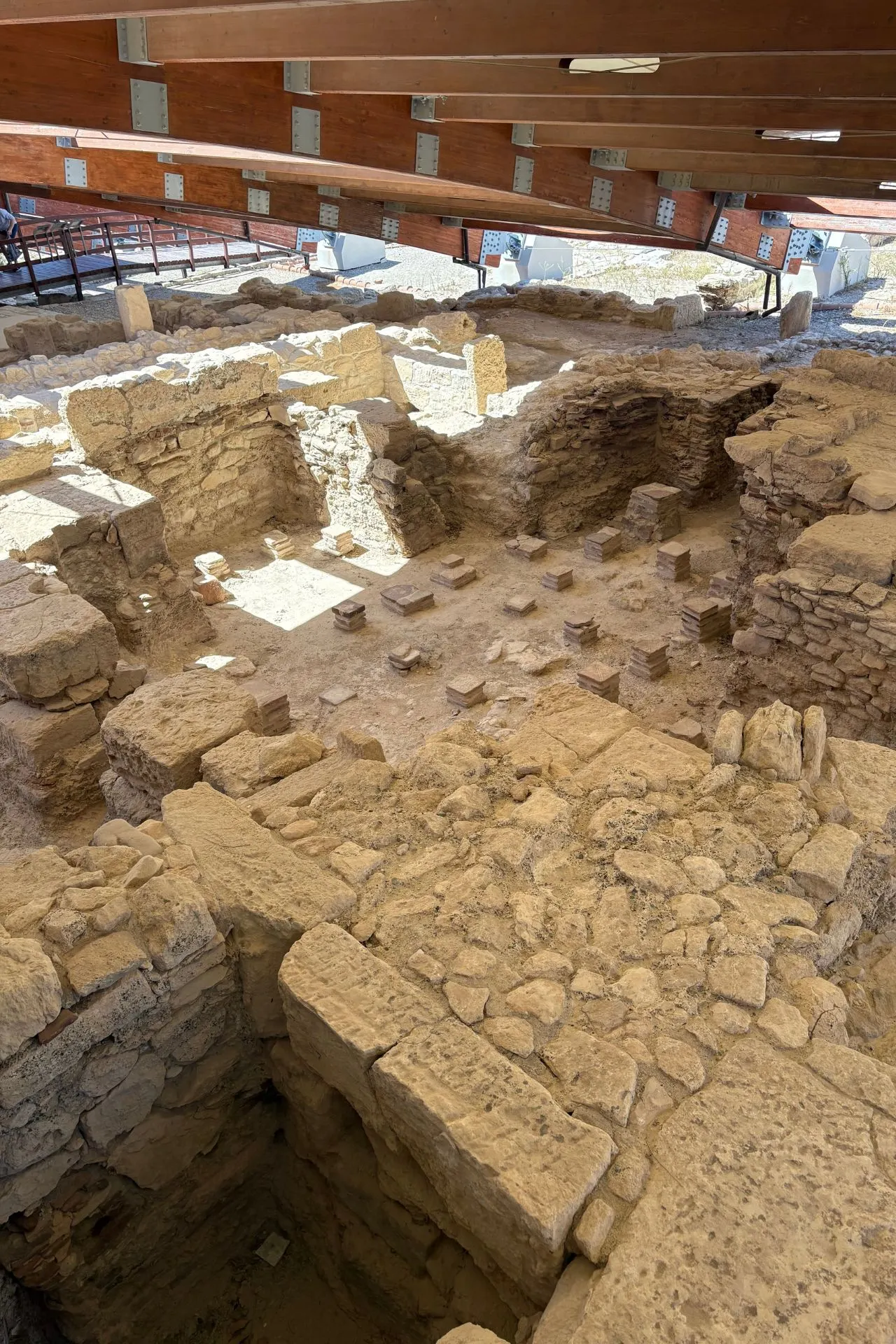 Archeologische opgravingen bij Kourion met zichtbare stenen muren en fundamenten onder een houten dakconstructie.