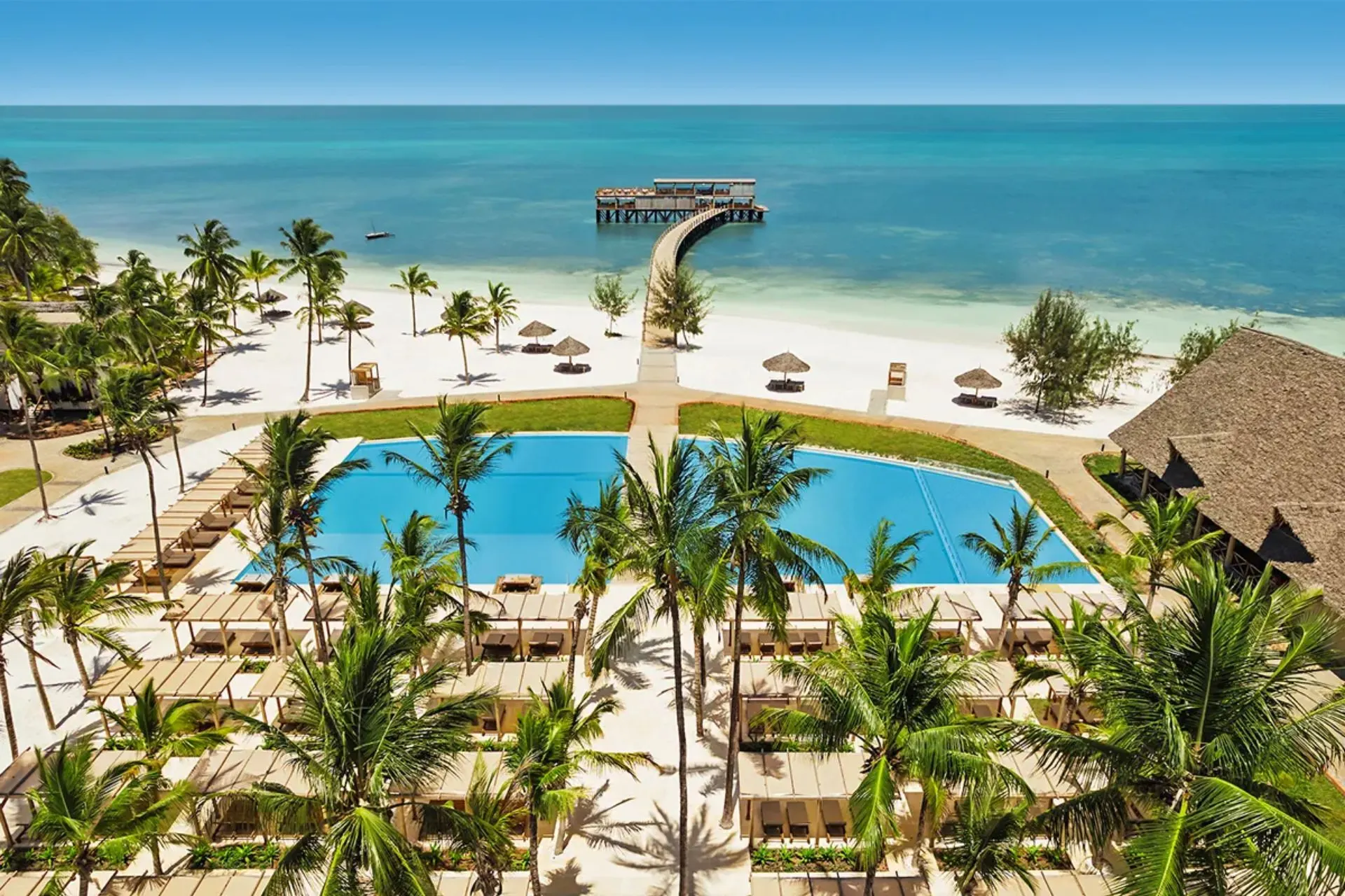 Overzicht van Jaz Elite Aurora Beach Resort in Michamvi op Zanzibar met een groot zwembad, tropische palmbomen, een wit zandstrand en de iconische pier die uitloopt in de Indische Oceaan. Dit luxe all-inclusive resort biedt rust, comfort en een prachtige ligging aan zee.