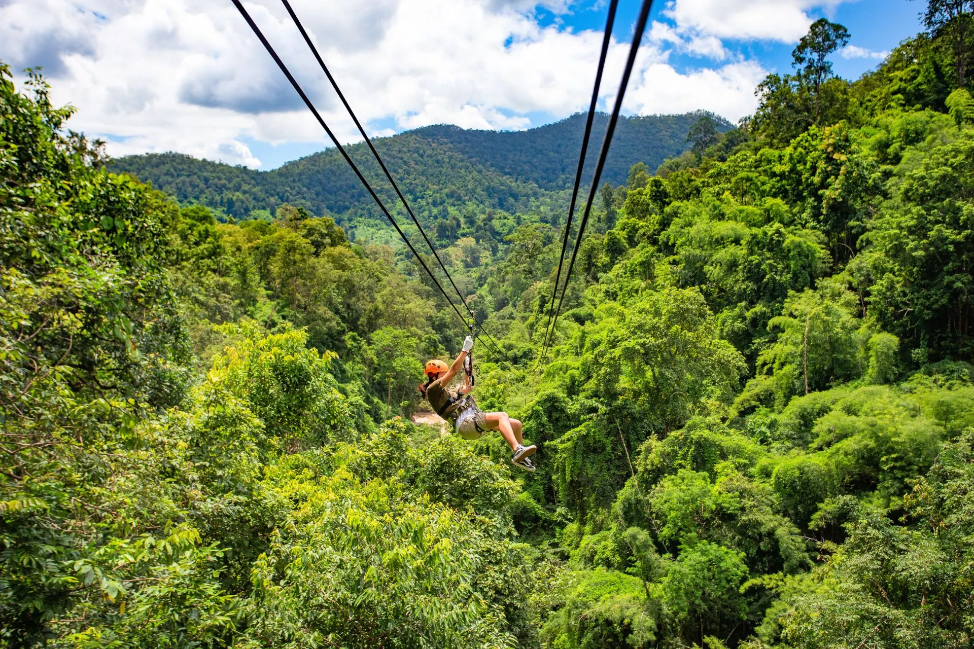 Avontuurlijke zipline-rit van een meisje hoog boven het weelderige Jamaicaanse landschap vol palmbomen en jungle.