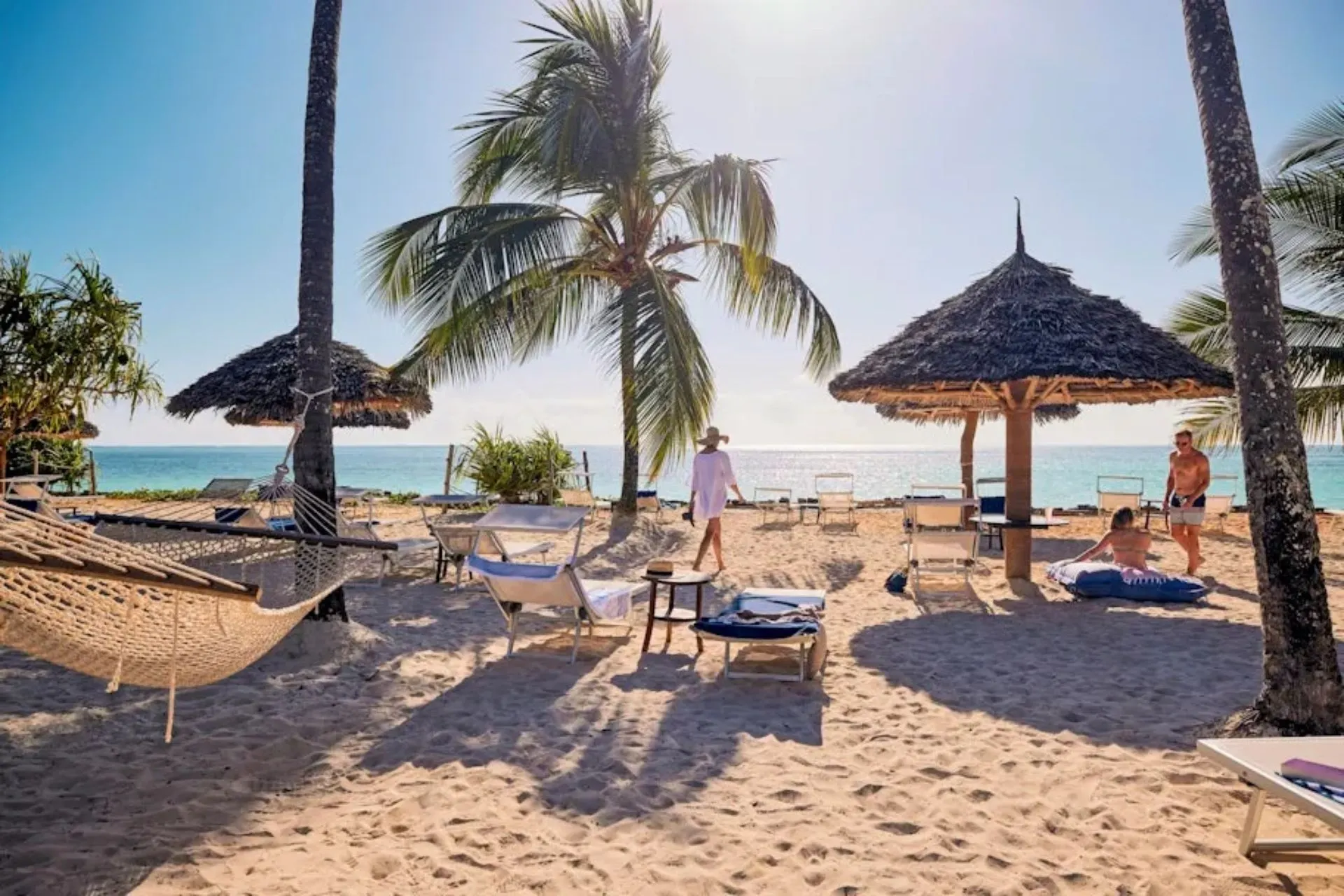 Strand van TUI BLUE Bahari Zanzibar met zacht wit zand, tropische palmbomen, hangmatten en rieten parasols. Gasten ontspannen direct aan de kust van Zanzibar terwijl ze genieten van het uitzicht over de helderblauwe Indische Oceaan. Een ideale locatie voor een ontspannen strandvakantie.