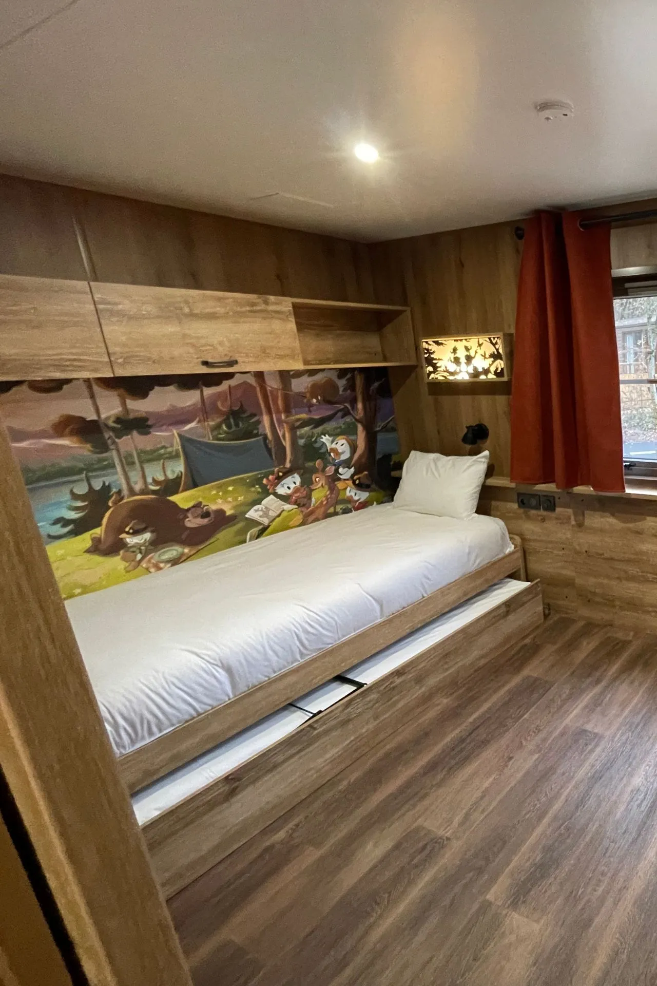 Sfeervolle kinderkamer in een bungalow van Davy Crockett Ranch bij Disneyland Parijs, met houten interieur, warme kleuren en een vrolijke Disney-muurschildering van Mickey en vrienden. Perfect voor gezinnen die comfort en Disney-magie willen combineren tijdens hun verblijf.