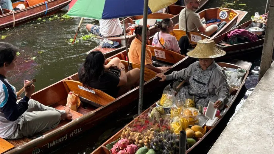 Traditionele houten boten op de drijvende markt van Damnoen Saduak, gevuld met kleurrijk tropisch fruit, terwijl verkopers en toeristen elkaar op het water ontmoeten.