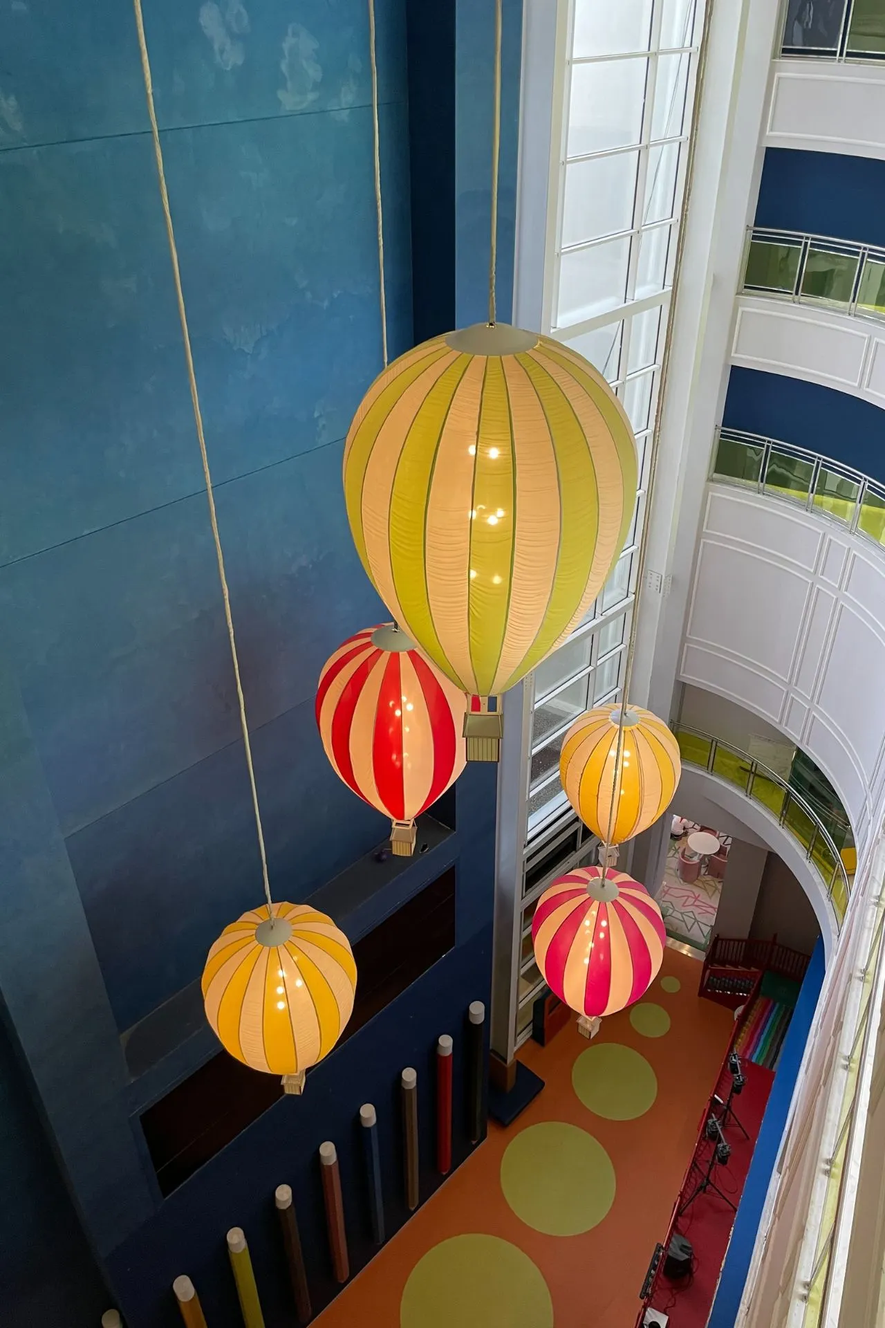 Binnenhal van het hotel met grote kleurrijke luchtballonlampen die aan het plafond hangen, boven een speels ingerichte ruimte.