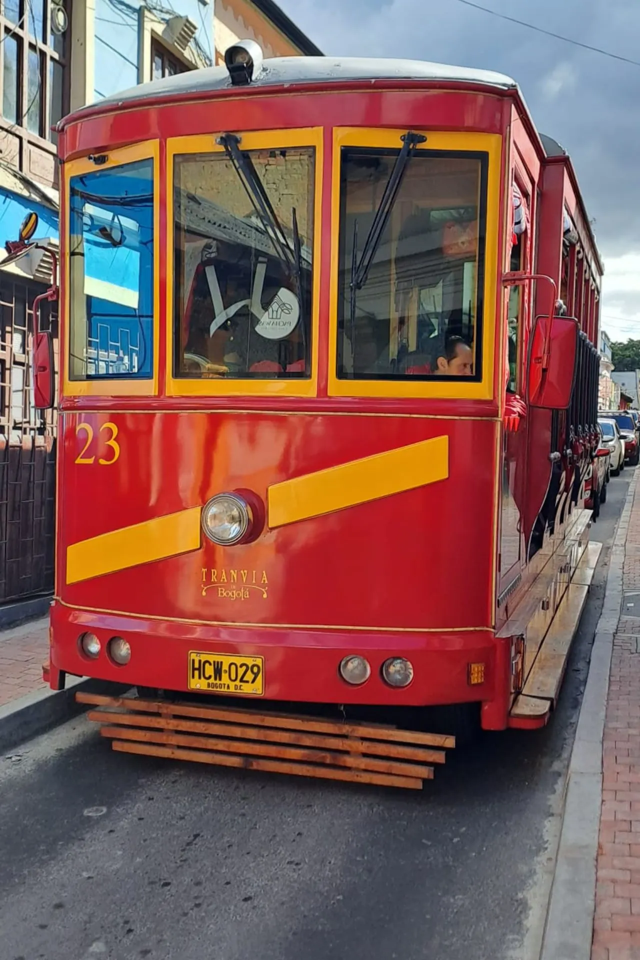 Rode historische tram met gele strepen en nummer 23, geparkeerd op een smalle straat met huizen op de achtergrond.