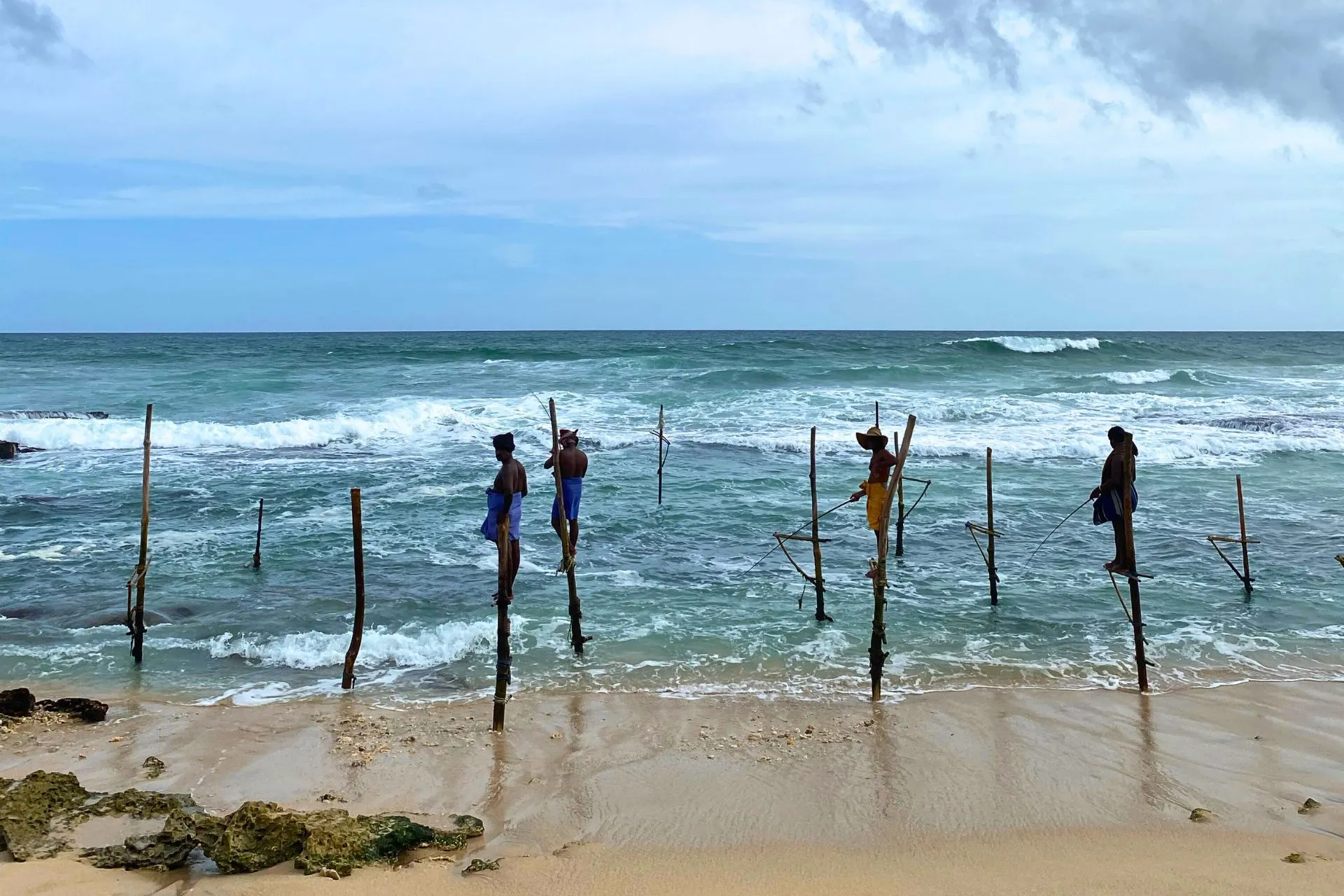 Traditionele paalvissers in Sri Lanka zittend op houten stokken in zee, vissend bij de branding.

