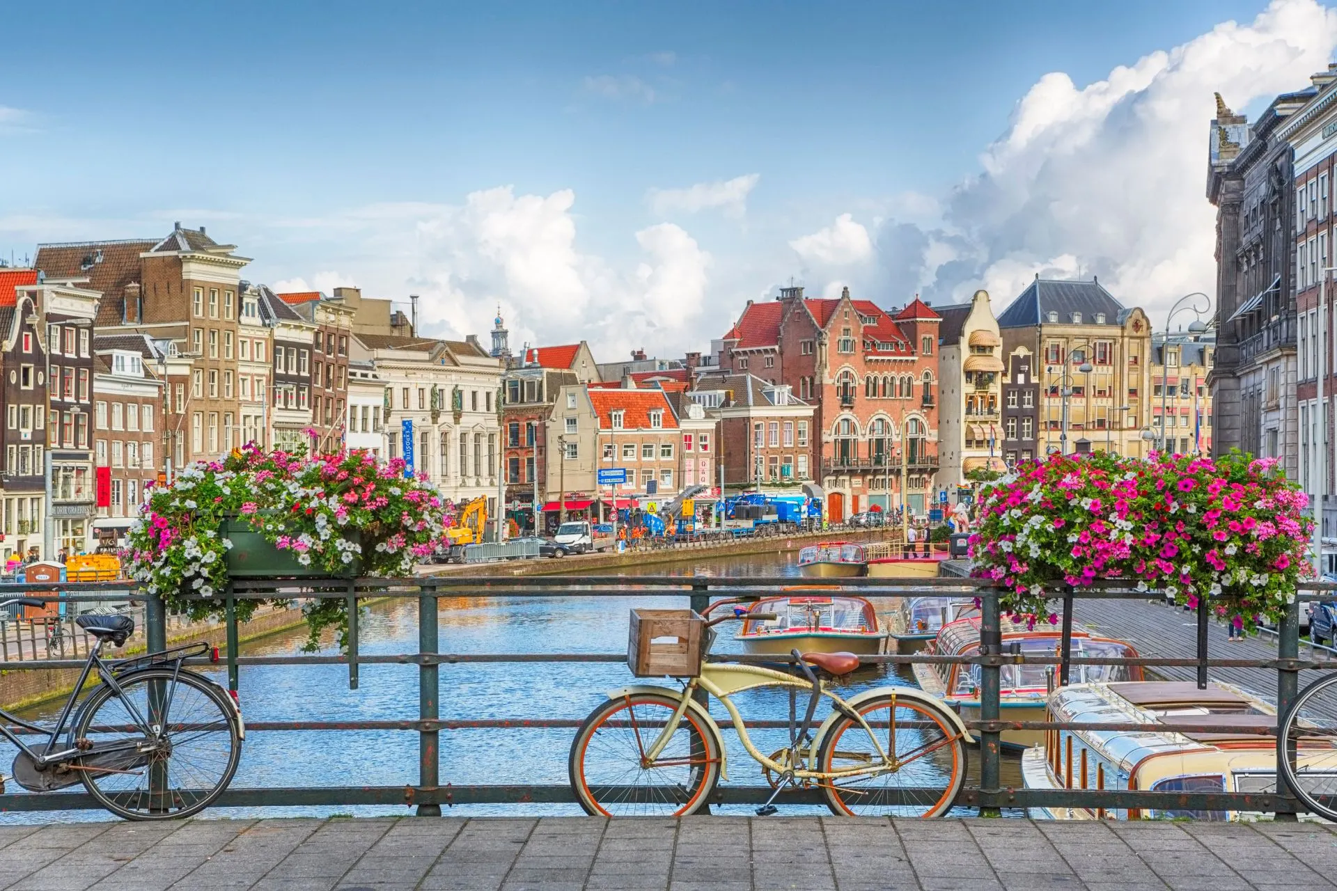 Zicht op een kleurrijke gracht in Amsterdam met fietsen op de voorgrond, bloembakken vol bloemen en historische grachtenpanden aan het water.