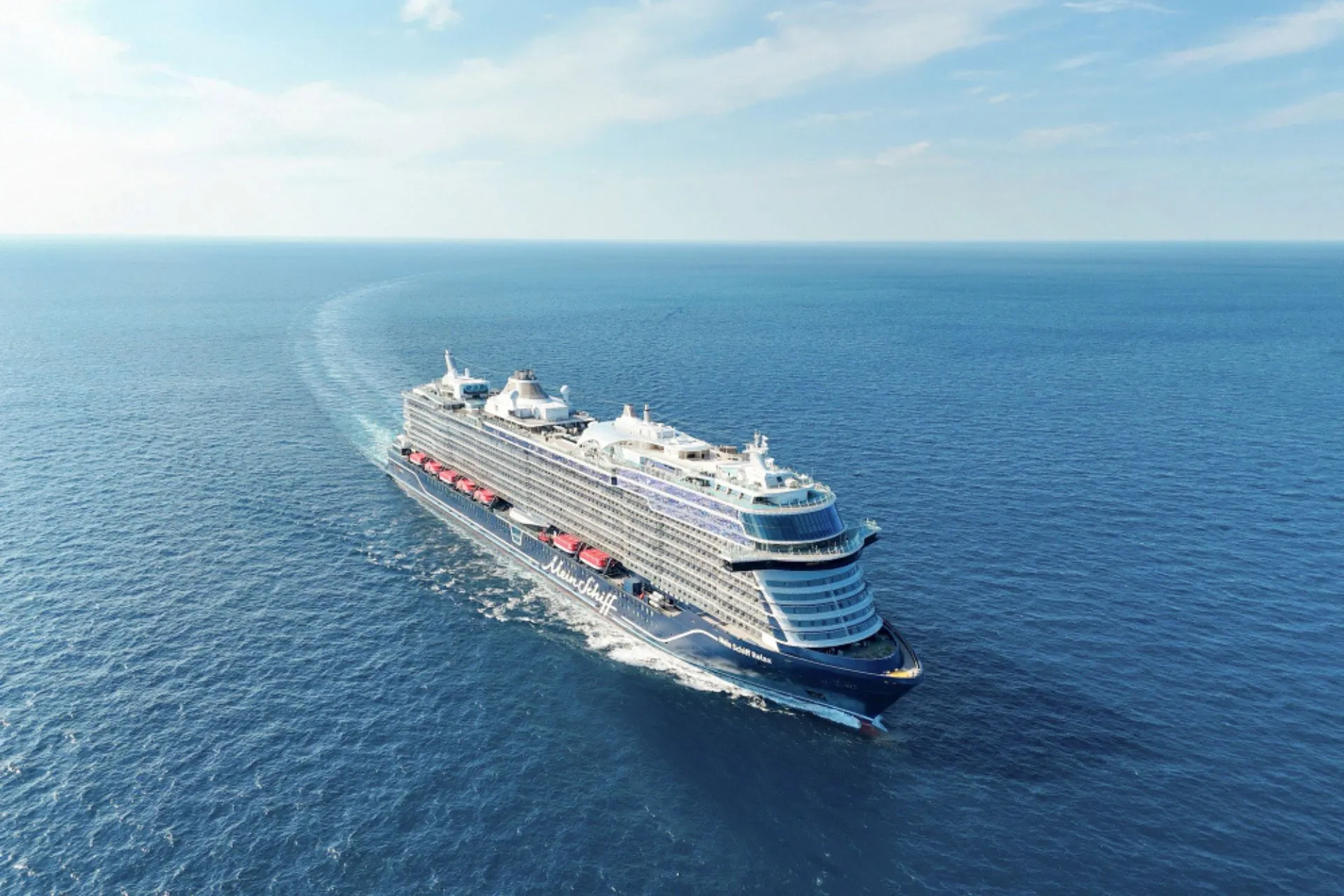 Luchtfoto van een Mein Schiff cruiseschip van TUI Cruises varend op open zee. Moderne schepen, duurzame innovaties en het Premium All Inclusive concept maken deze cruise ideaal voor een zorgeloze vakantie.
