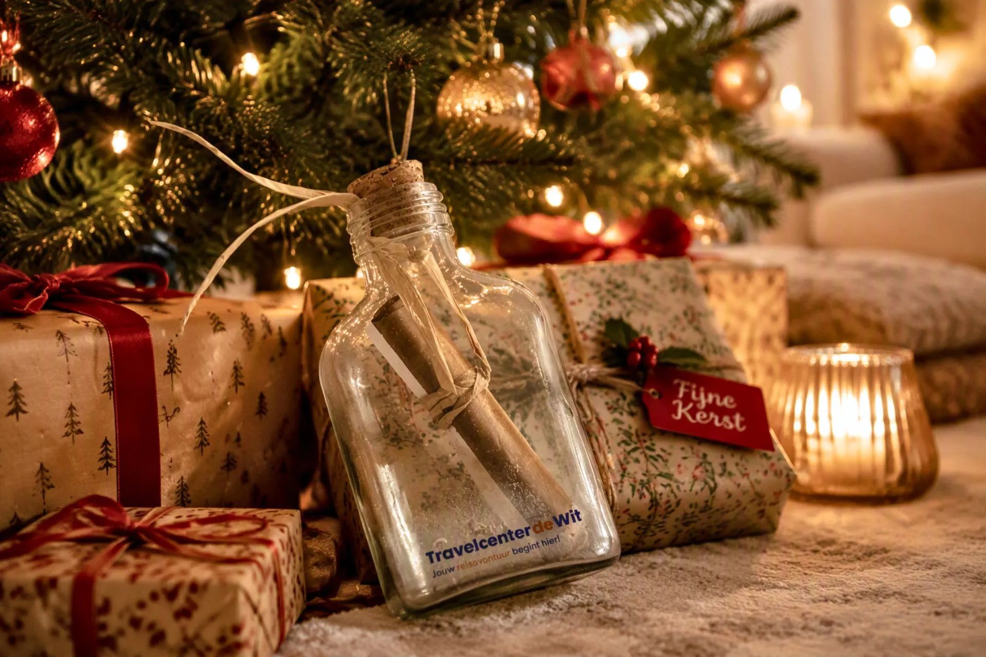 Reischeque van Travelcenter de Wit in een glazen fles met fijn zand en schelpjes, geplaatst voor een sfeervol versierde kerstboom met cadeaus. Een origineel cadeau voor Kerstmis, een verjaardag of speciale gelegenheid waarmee je een vakantie of reis cadeau geeft.