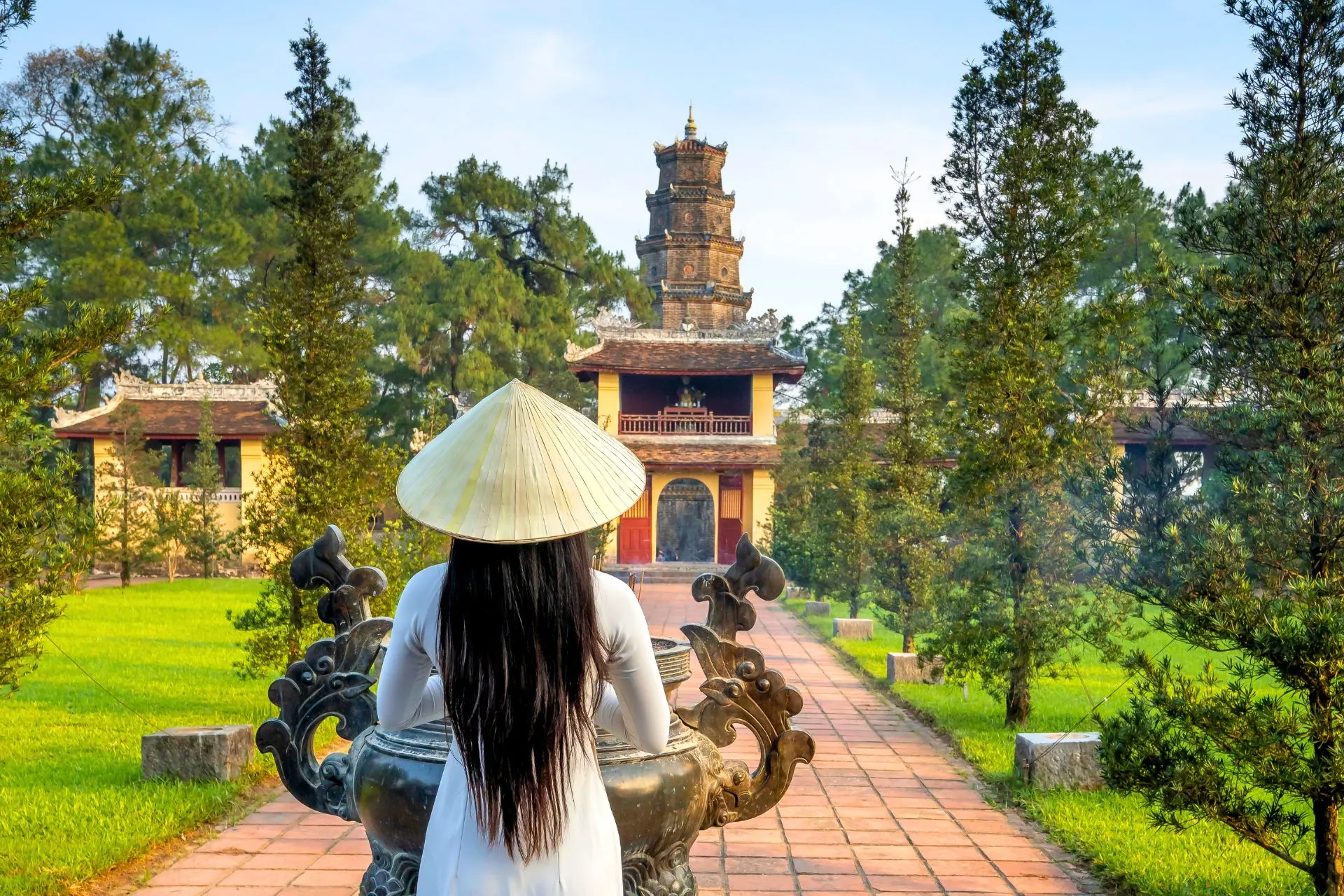Vrouw met hoed en lang zwart haar lopend naar een tempel in Vietnam