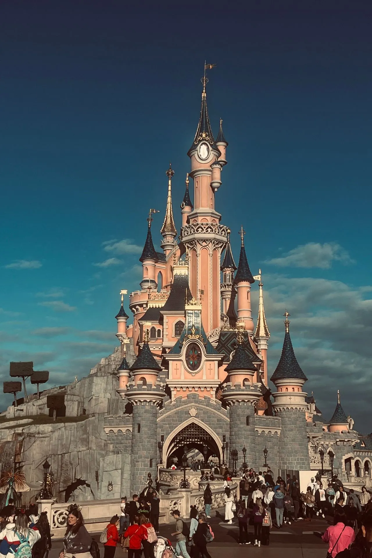 Het iconische Doornroosje kasteel in Disneyland Parijs, omringd door bezoekers op een zonnige dag met een blauwe lucht en lichte wolken.
