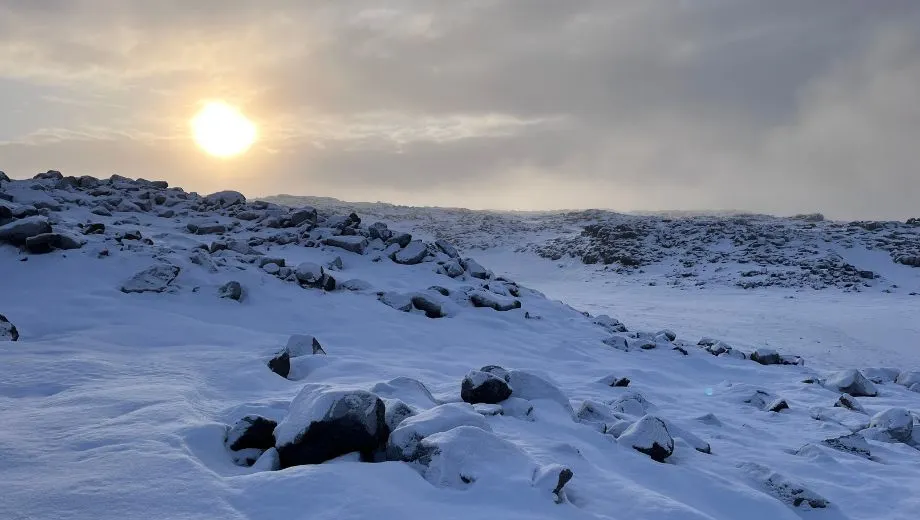 Winterlandschap in Noord‑IJsland met rotsen en sneeuwvelden bij lage winterzon.
