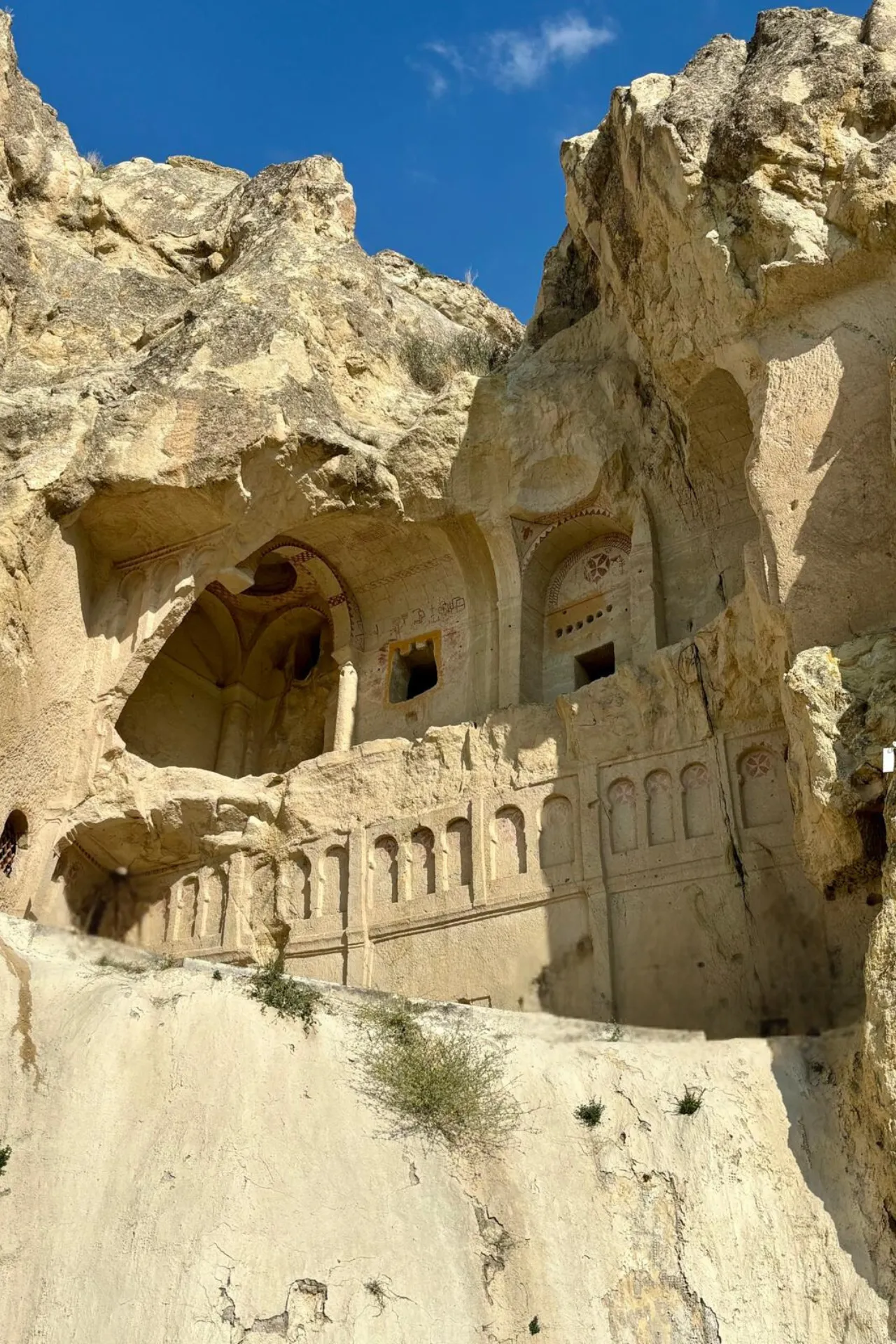 Historische rotskerk in Cappadocië, Turkije, uitgehouwen in zacht vulkanisch gesteente met gedetailleerde bogen en nissen die eeuwenoude architectuur tonen. De façade bevat decoratieve elementen en ramen, terwijl de natuurlijke rotsformaties eromheen een indrukwekkend contrast vormen. Deze unieke locatie maakt deel uit van het UNESCO-werelderfgoed en is een populaire bestemming voor reizigers die op zoek zijn naar cultuur, geschiedenis en bijzondere bezienswaardigheden in Anatolië.