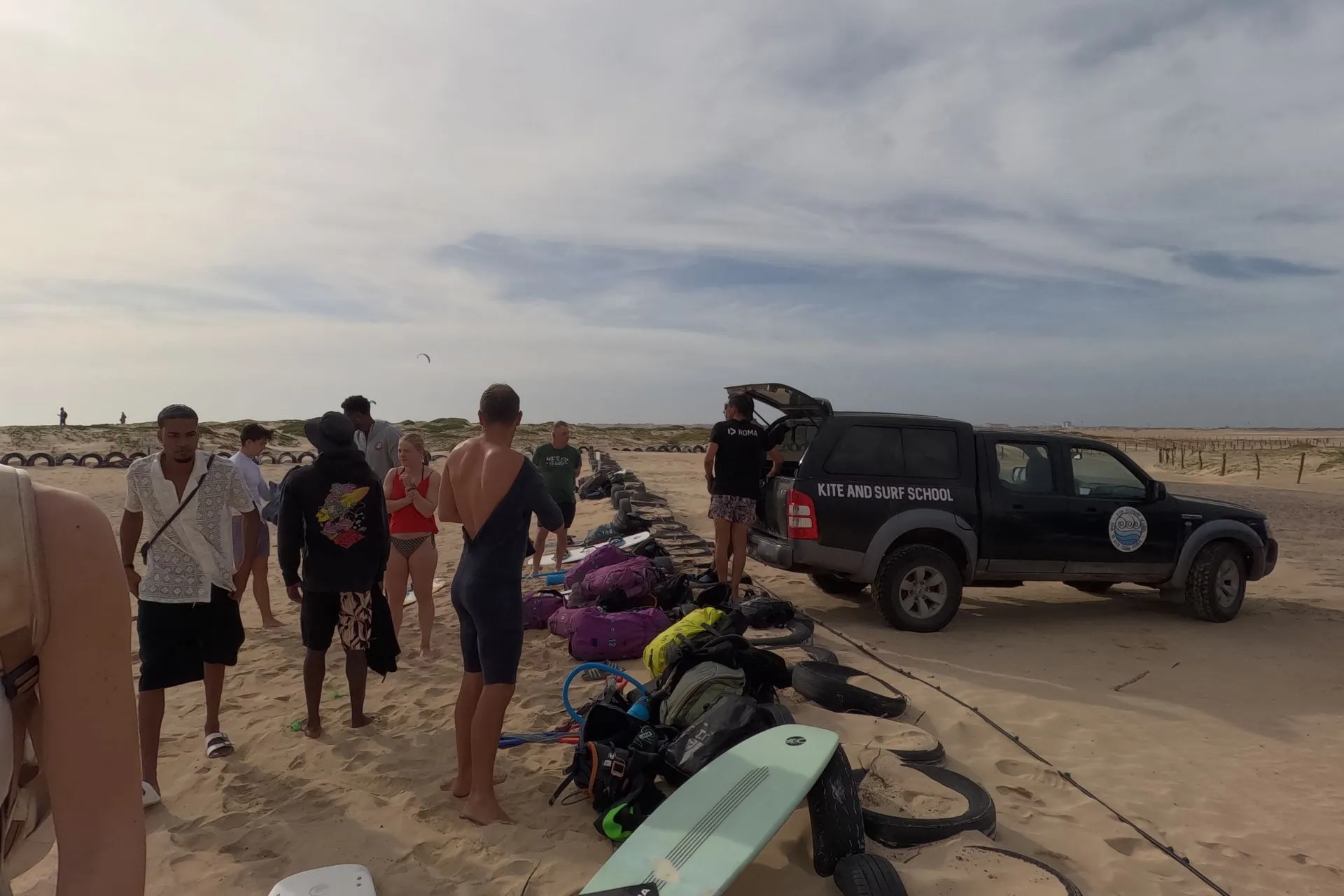 Groep reizigers verzameld op een breed zandstrand op Kaapverdië naast een kite- en surfschool, met surfmateriaal, boards en een begeleidende wagen in de omgeving. De ontspannen sfeer en voorbereiding op watersport benadrukken hoe geliefd Kaapverdië is bij sportieve vakantiegangers. Dit beeld sluit goed aan bij een zonvakantie Kaapverdië gecombineerd met actie, waarbij kitesurfen en strandactiviteiten een belangrijk onderdeel vormen van het eilandgevoel.

