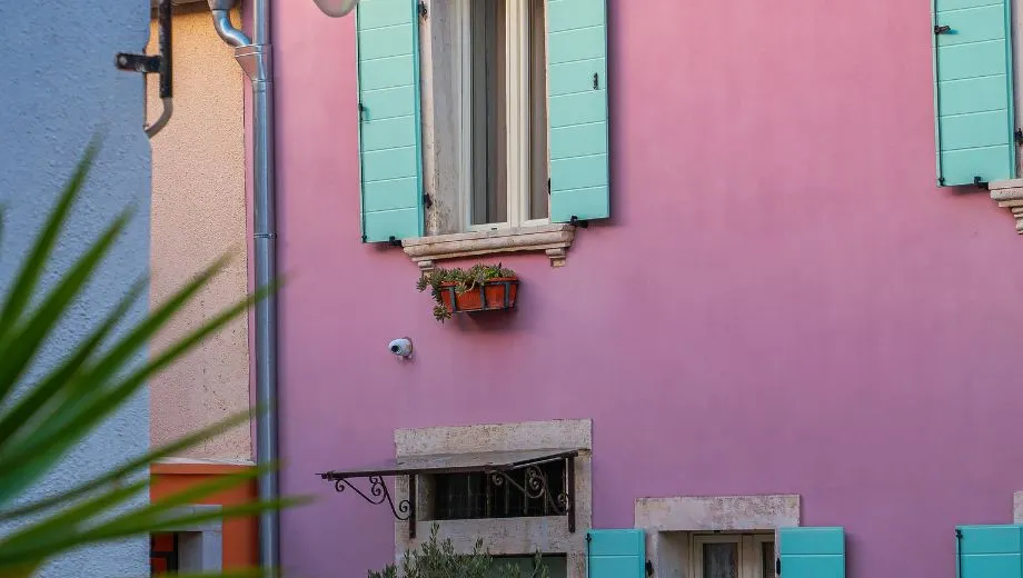 "Close-up van een kleurrijke gevel in Istrië, Kroatië, met pastelroze muren en turquoise luiken, typisch voor mediterrane architectuur. Deze charmante details weerspiegelen de authentieke sfeer van Kroatische kustplaatsen. Perfect voor fotografie, cultuur en ontspanning. Ontdek pittoreske straatjes, lokale gastronomie en historische charme tijdens een vakantie in Istrië."