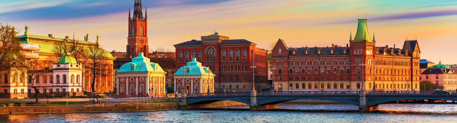 Stad aan het water met een warme oranje gloed van de zonsondergang die weerspiegelt in het rustige water.