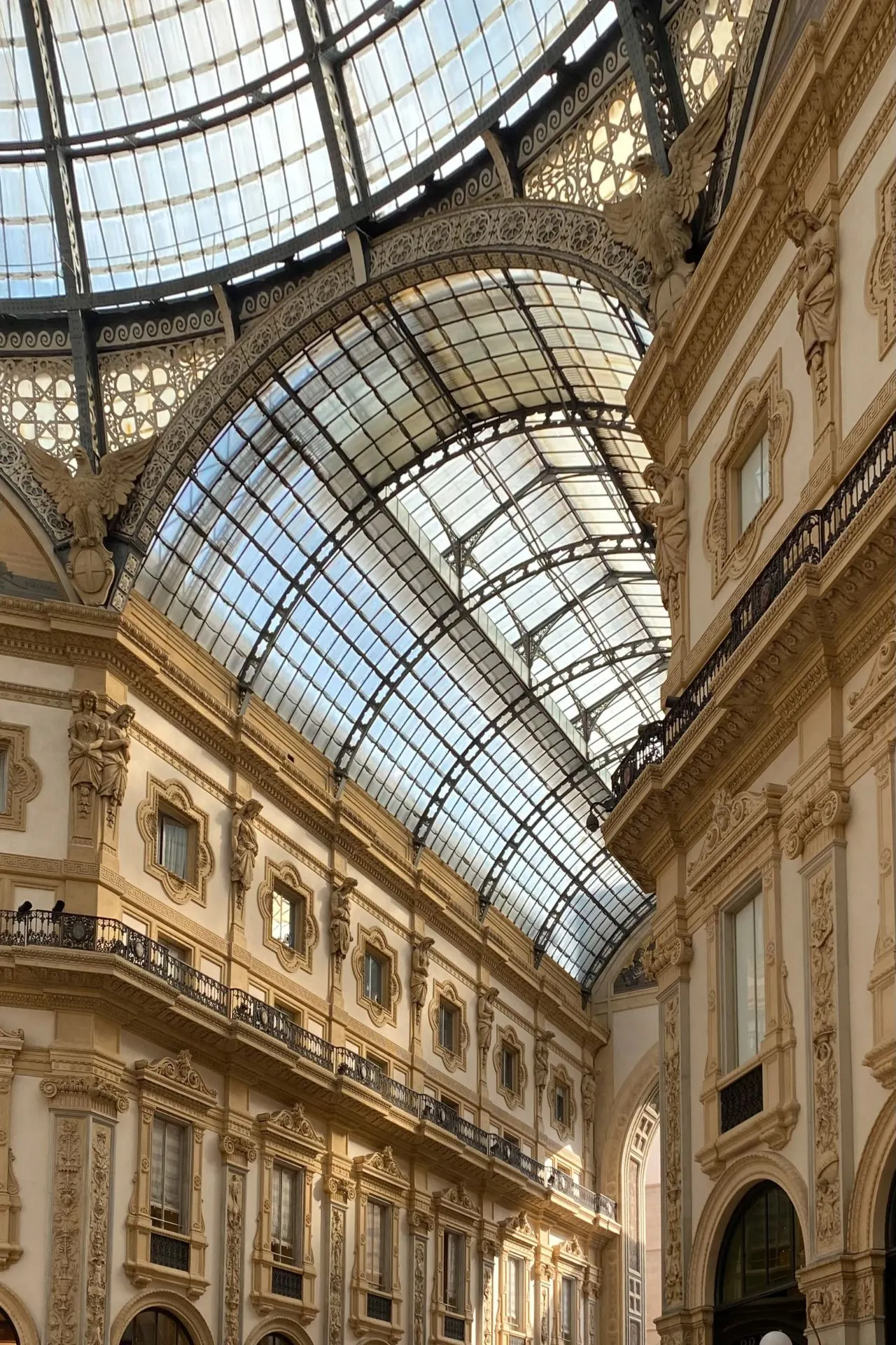 Binnenzicht in de Galleria Vittorio Emanuele II met de indrukwekkende glazen koepel, omlijst door klassieke gevels en muurschilderingen met allegorische figuren.
