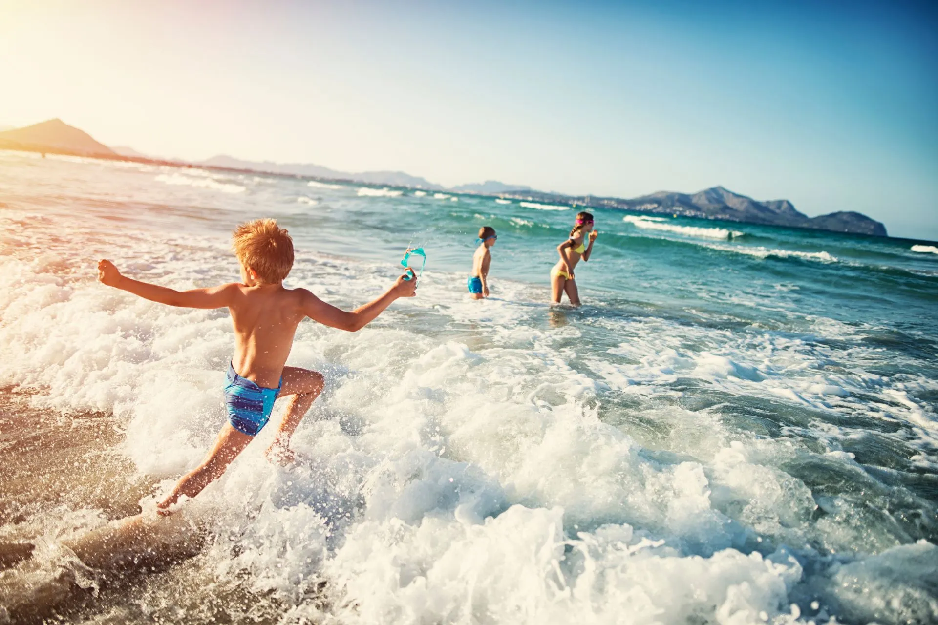 Drie kinderen spelen in de zee tijdens een zonnige familievakantie – een vrolijk moment van een kindvriendelijke all-inclusive zomervakantie in 2026, geboekt met vroegboekvoordeel via Travelcenter de Wit.