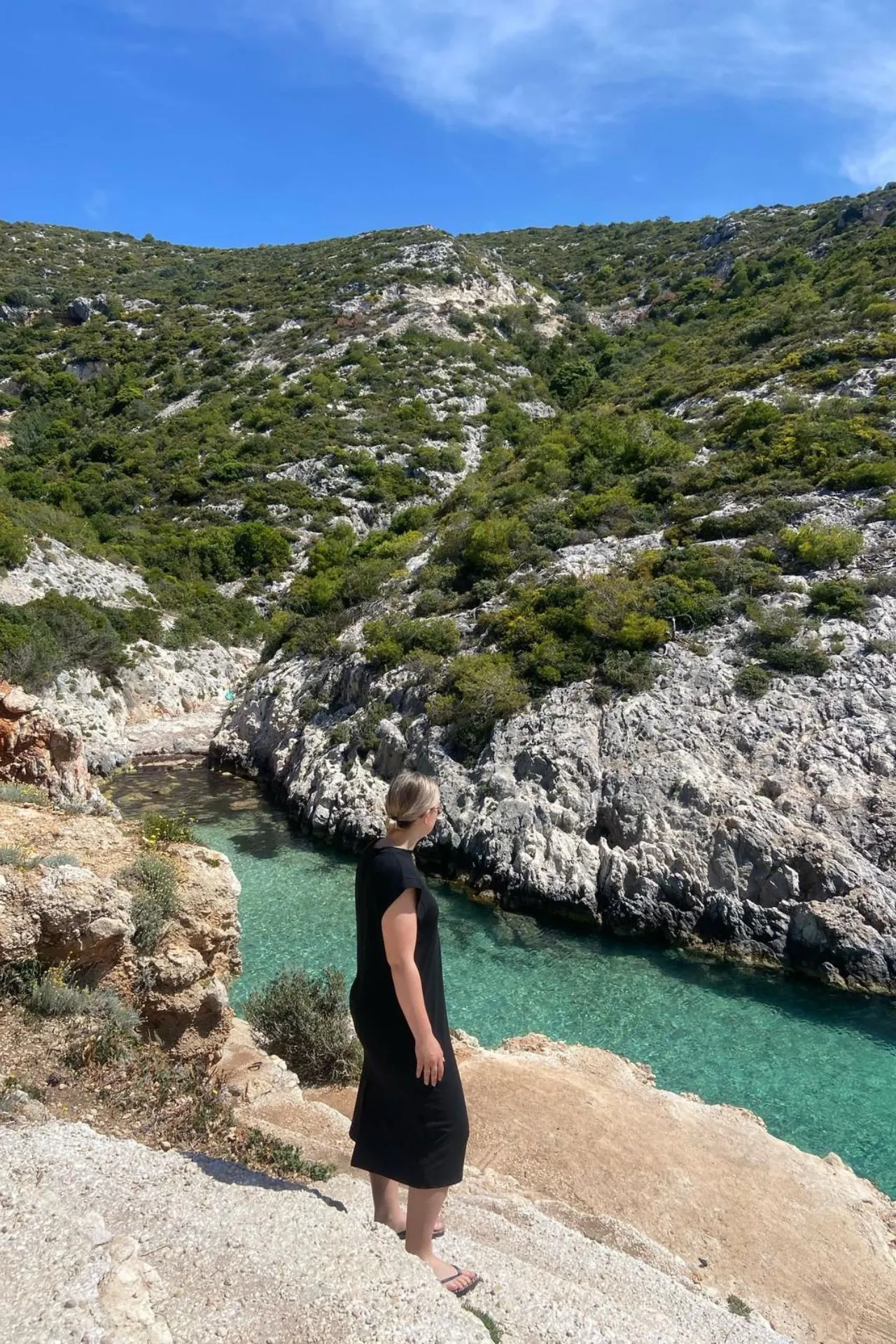 Persoon kijkt uit over een smalle baai met helder turquoise water en rotsachtige heuvels op Zakynthos. 