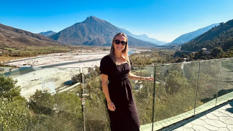 Reisadviseur Floor poseert op een panoramisch uitkijkpunt met een adembenemend uitzicht over bergen en een rivier in Albanië.