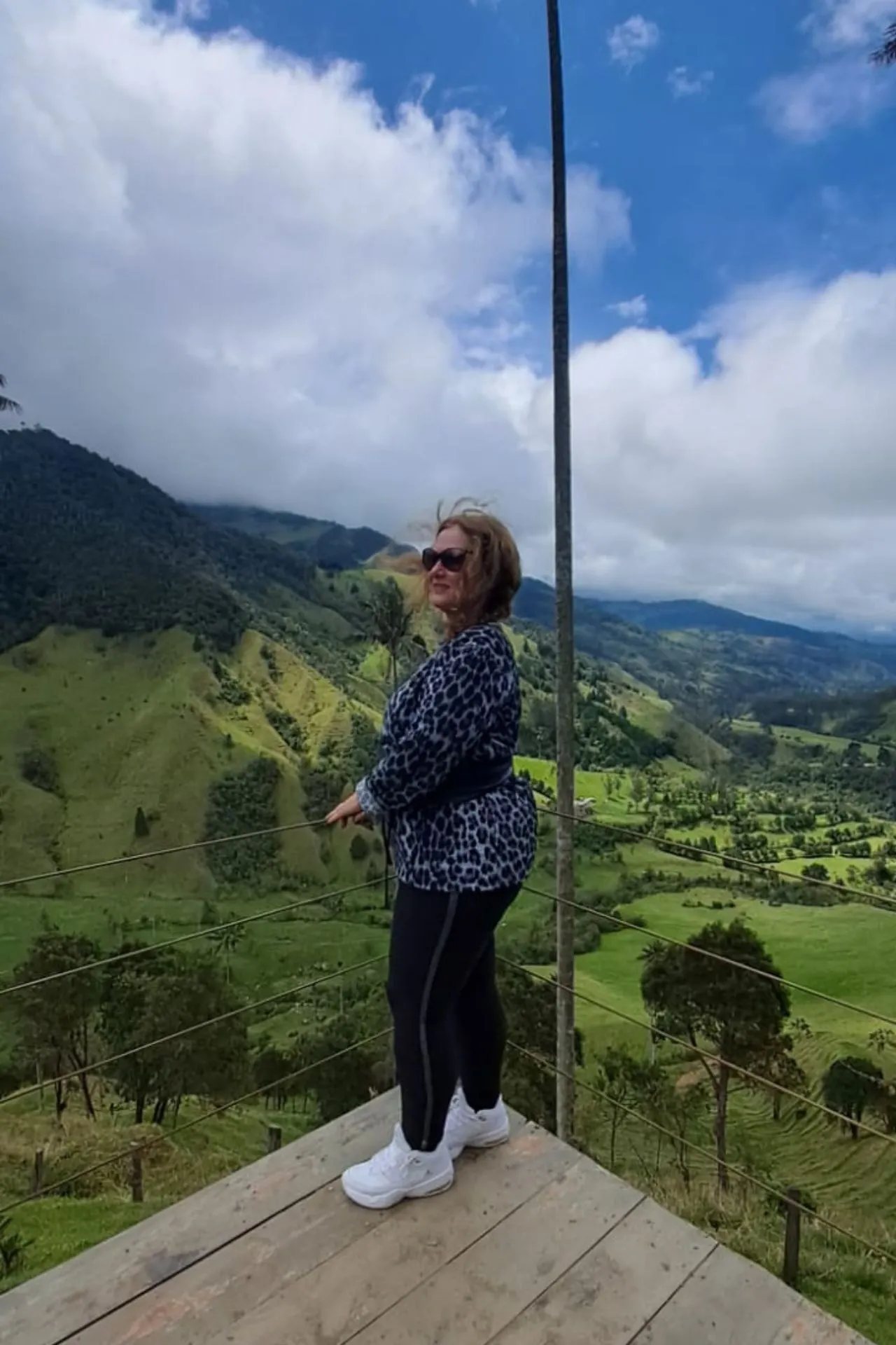 Uitzichtpunt met groene bergen en valleien onder een deels bewolkte lucht, gezien vanaf een houten platform.