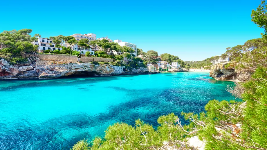 "Adembenemende baai op Mallorca, Balearen, Spanje, met kristalhelder turquoise water, rotsachtige kliffen en mediterrane vegetatie onder een stralende blauwe lucht. Luxe villa’s en hotels liggen langs de kust, ideaal voor zonvakantie, zwemmen en ontspanning. Ontdek verborgen stranden, pittoreske landschappen en het authentieke karakter van dit populaire vakantie-eiland in de Middellandse Zee."

Deze afbeelding toont een schitterende baai met helder turquoise water, omringd door groene pijnbomen en sfeervolle witte gebouwen op de rotsen. Dit is het perfecte decor voor een zonvakantie Verasole, waar ontspanning en genieten centraal staan. Op de achtergrond zie je charmante hotels en appartementen, ideaal voor een Verasole vakantie aan de Middellandse Zee. De zon schijnt fel en de lucht is strakblauw, wat direct het vakantiegevoel oproept. Deze locatie is zeer geschikt voor een pakketreis Verasole, waarbij vlucht en accommodatie volledig zijn geregeld. Of je nu kiest voor een romantische vakantie, een gezinsuitje of een luxe verblijf, bij Verasole vind je altijd de ideale zonbestemming. Deze afbeelding benadrukt het gemak en de sfeer van Verasole vakanties: alles is tot in de puntjes verzorgd, zodat je zorgeloos kunt genieten van een onvergetelijke vakantie aan het water.