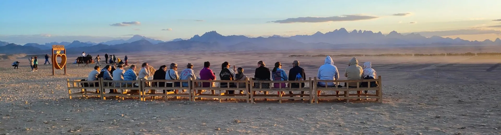 Groep reizigers zit op houten banken en kijkt uit over de Egyptische woestijn met bergen tijdens zonsondergang. El Gouna en Hurghada 