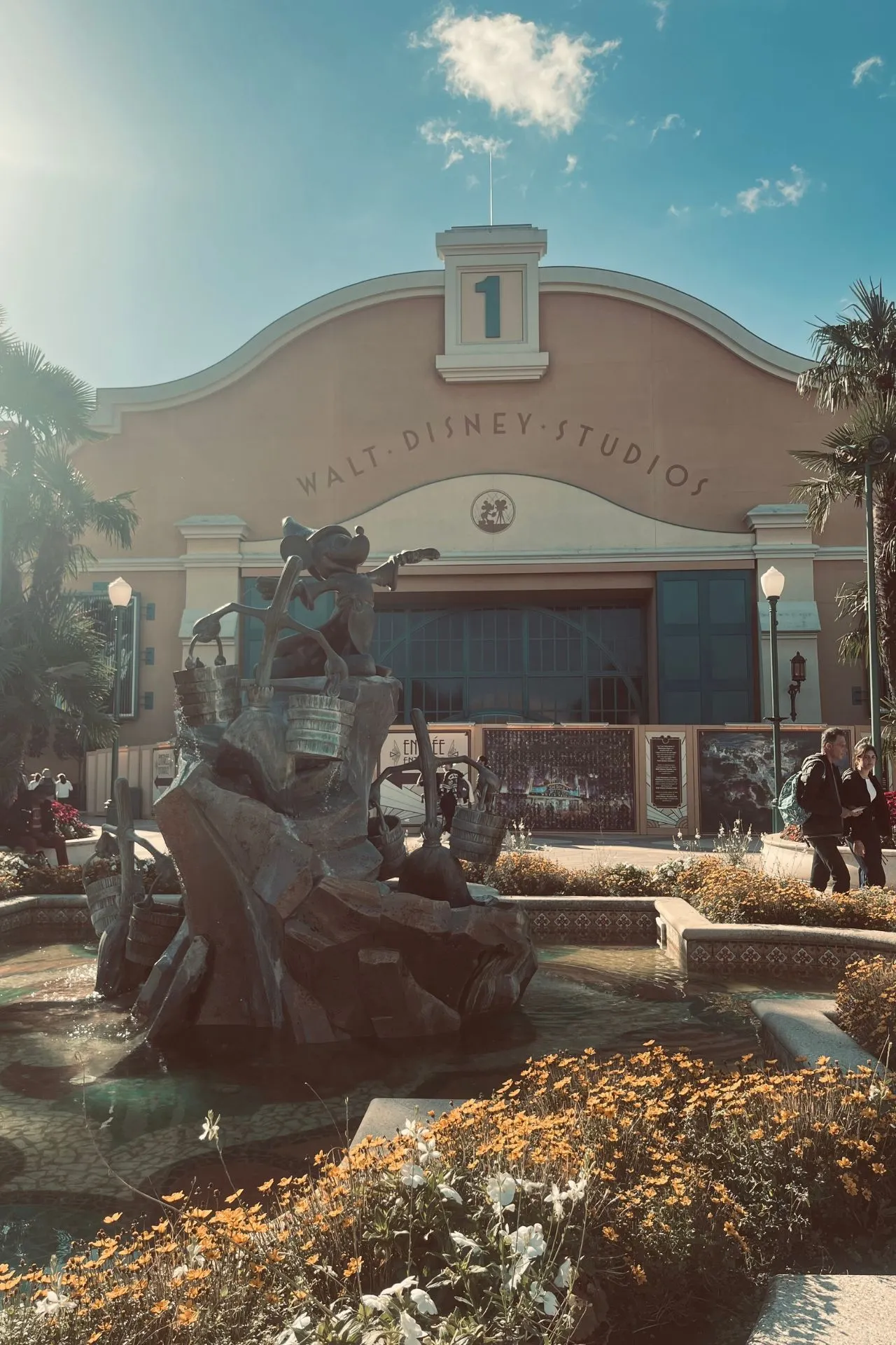 Ingang van Walt Disney Studios Park in Disneyland Parijs met het iconische gebouw van Studio 1 en een fontein met Disney-figuren op een zonnige dag.